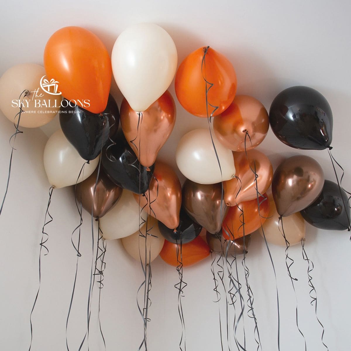 Orange, black, cream and metallic copper-toned helium ceiling balloons with hanging black curling ribbons.