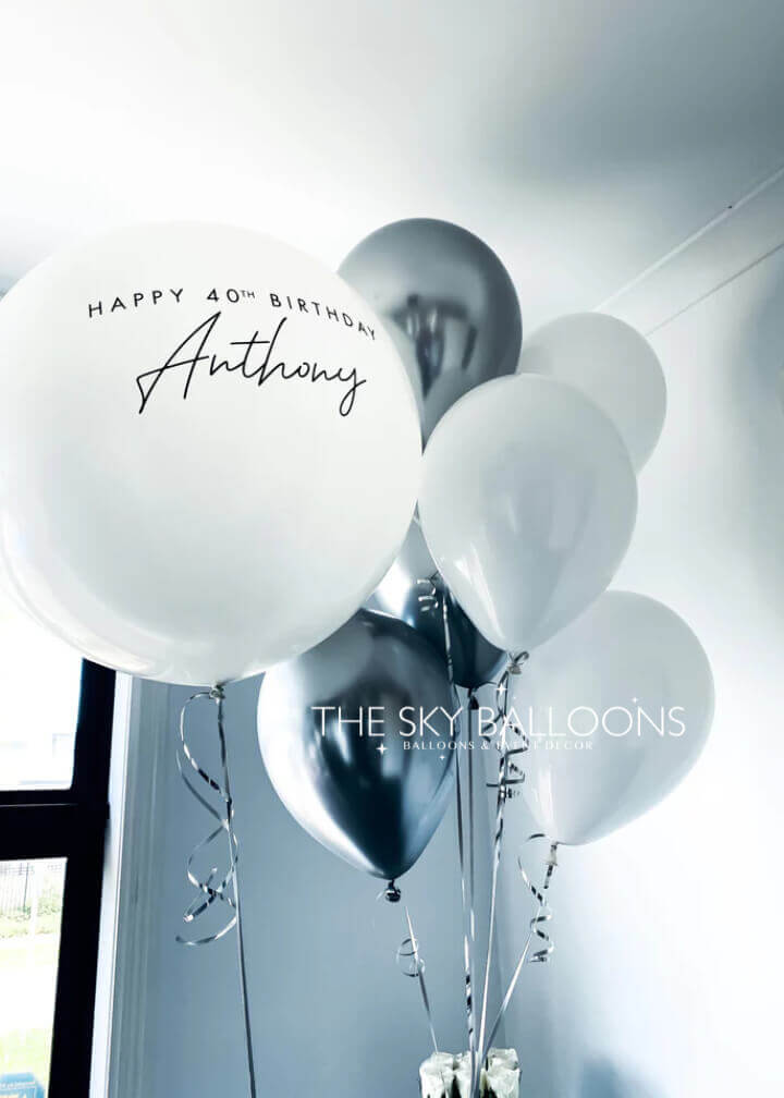 A set of balloons including white and black balloons with one personalized balloon that reads 'Happy 40th Birthday Anthony'.