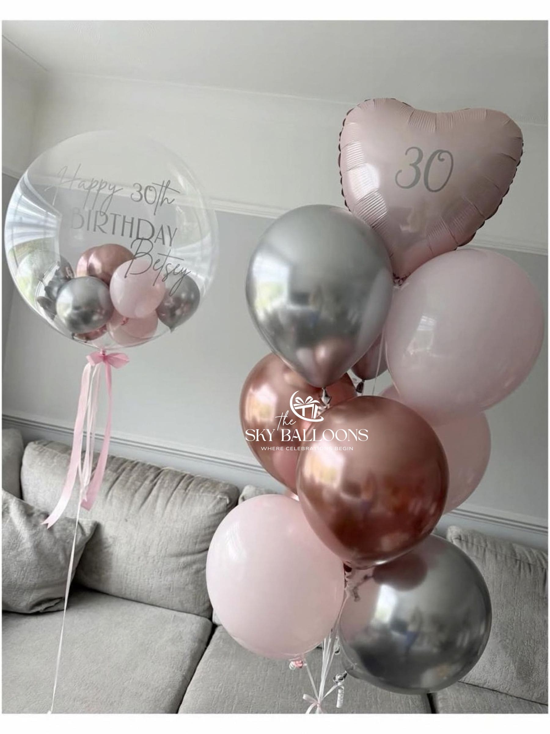 Personalised birthday bubble balloon with mini balloons inside, beside a blush-pink heart foil and pink, rose-gold and silver latex balloons.