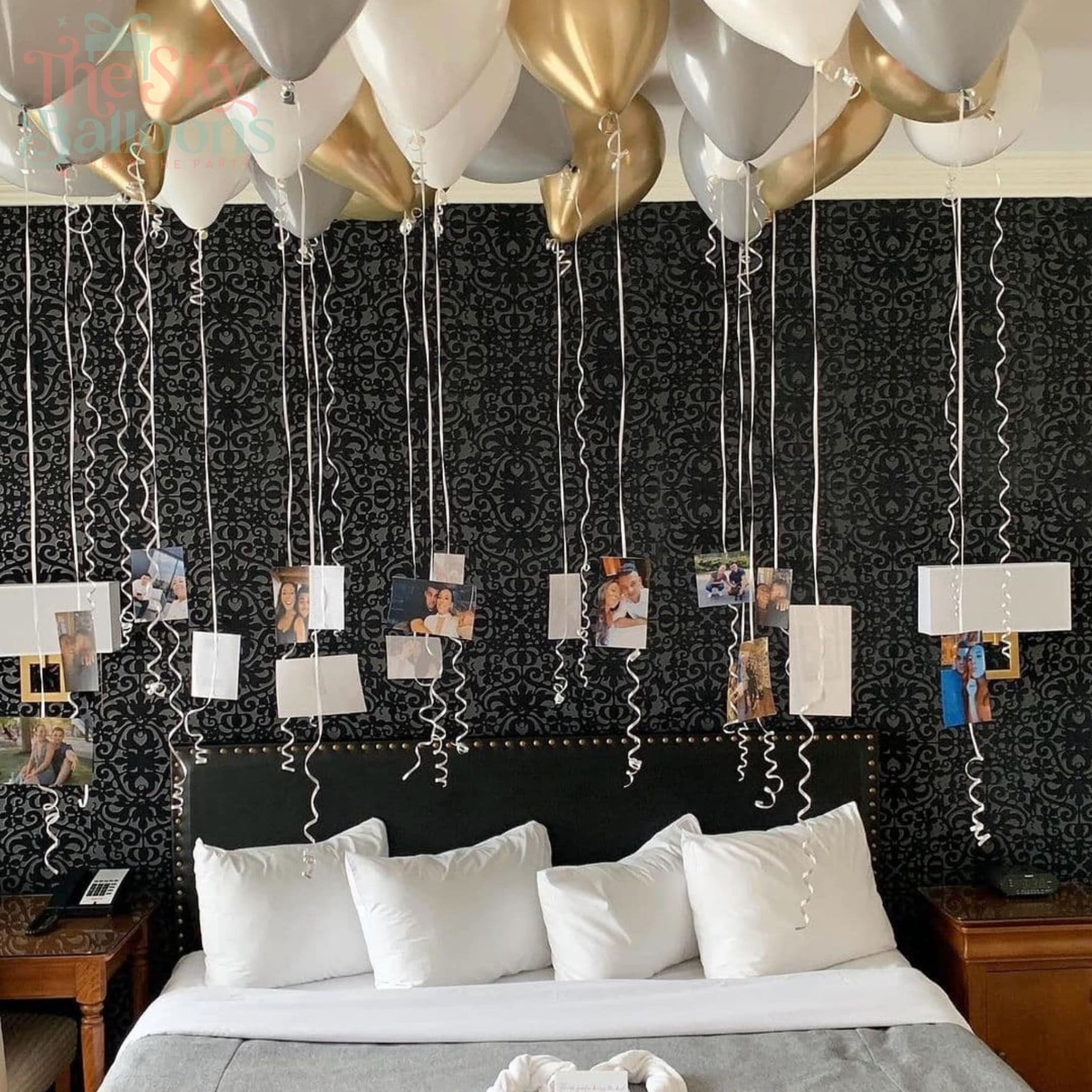 Decorative setup with balloons and photo streamers on a bed in a room.