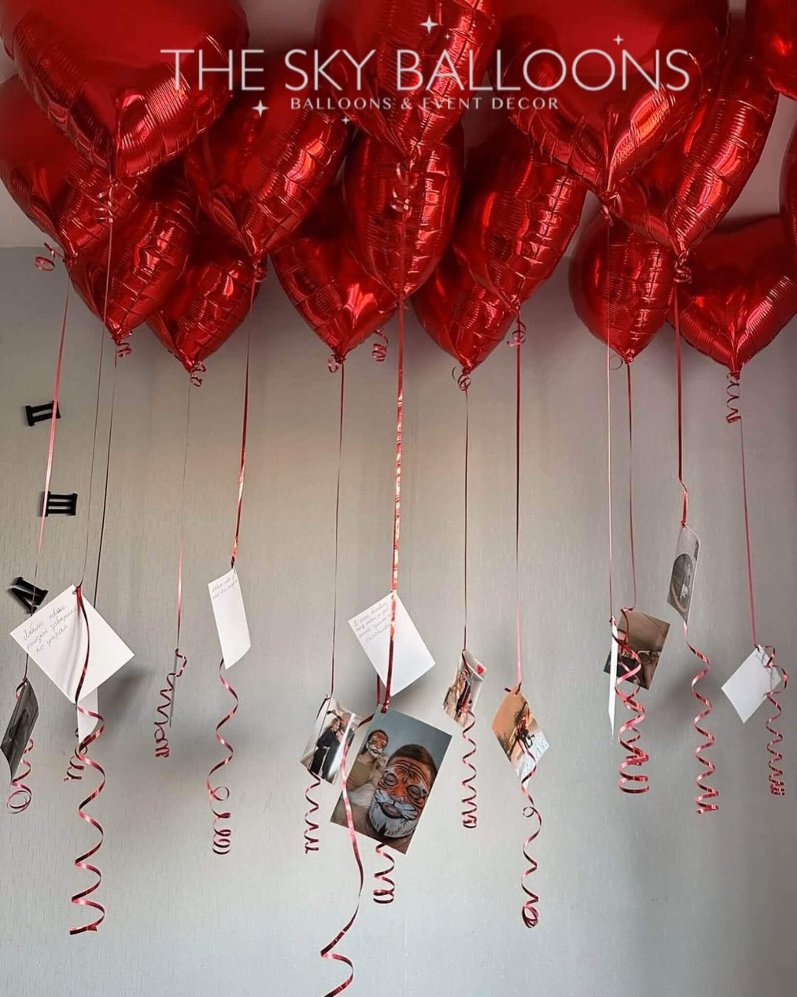 A beautiful arrangement of red heart-shaped helium balloons with attached photo prints and message cards, creating a sentimental and decorative floating display. Perfect for special occasions like birthdays, anniversaries, and romantic surprises.
