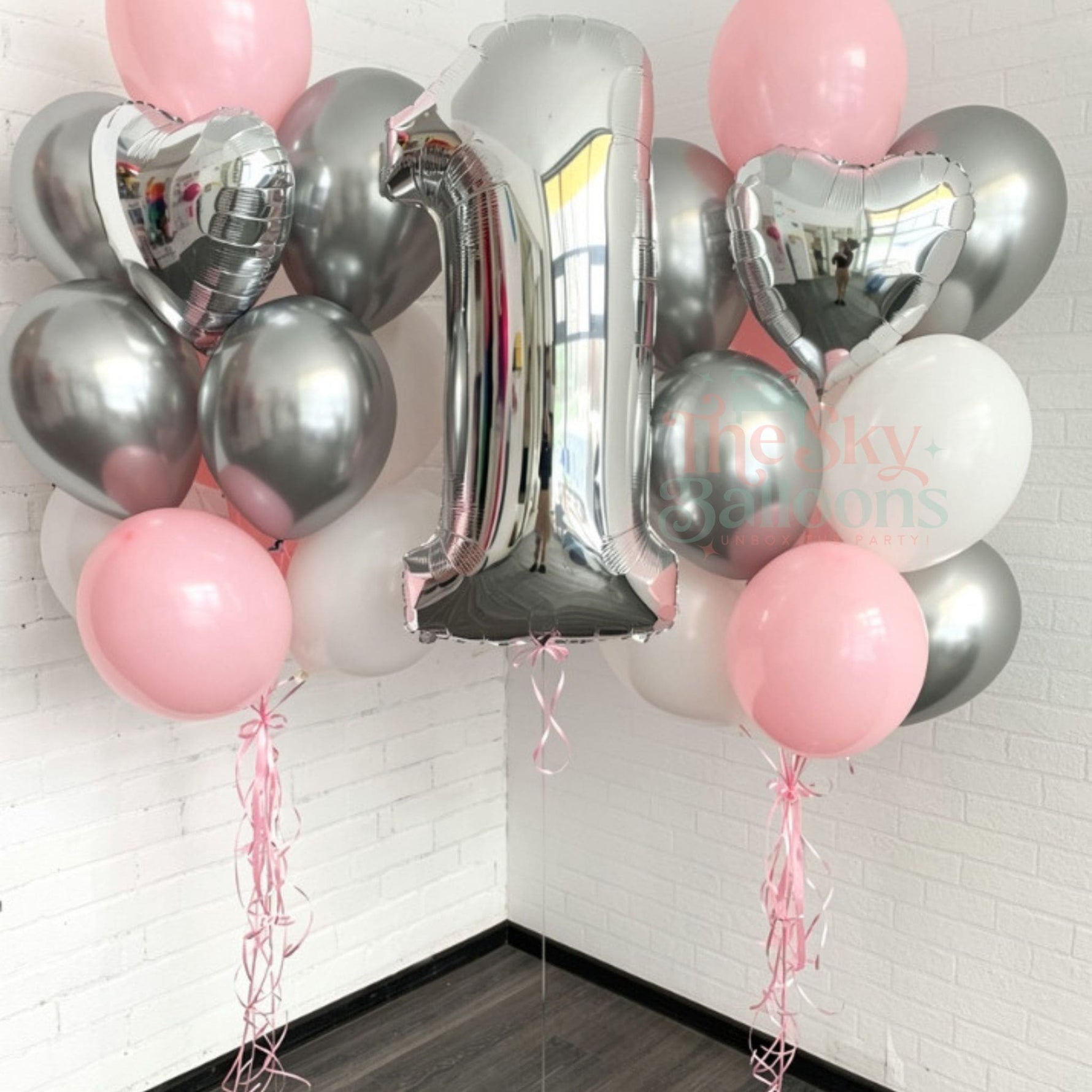 Bouquet of pink and silver balloons with a number 1 balloon against a white brick wall.