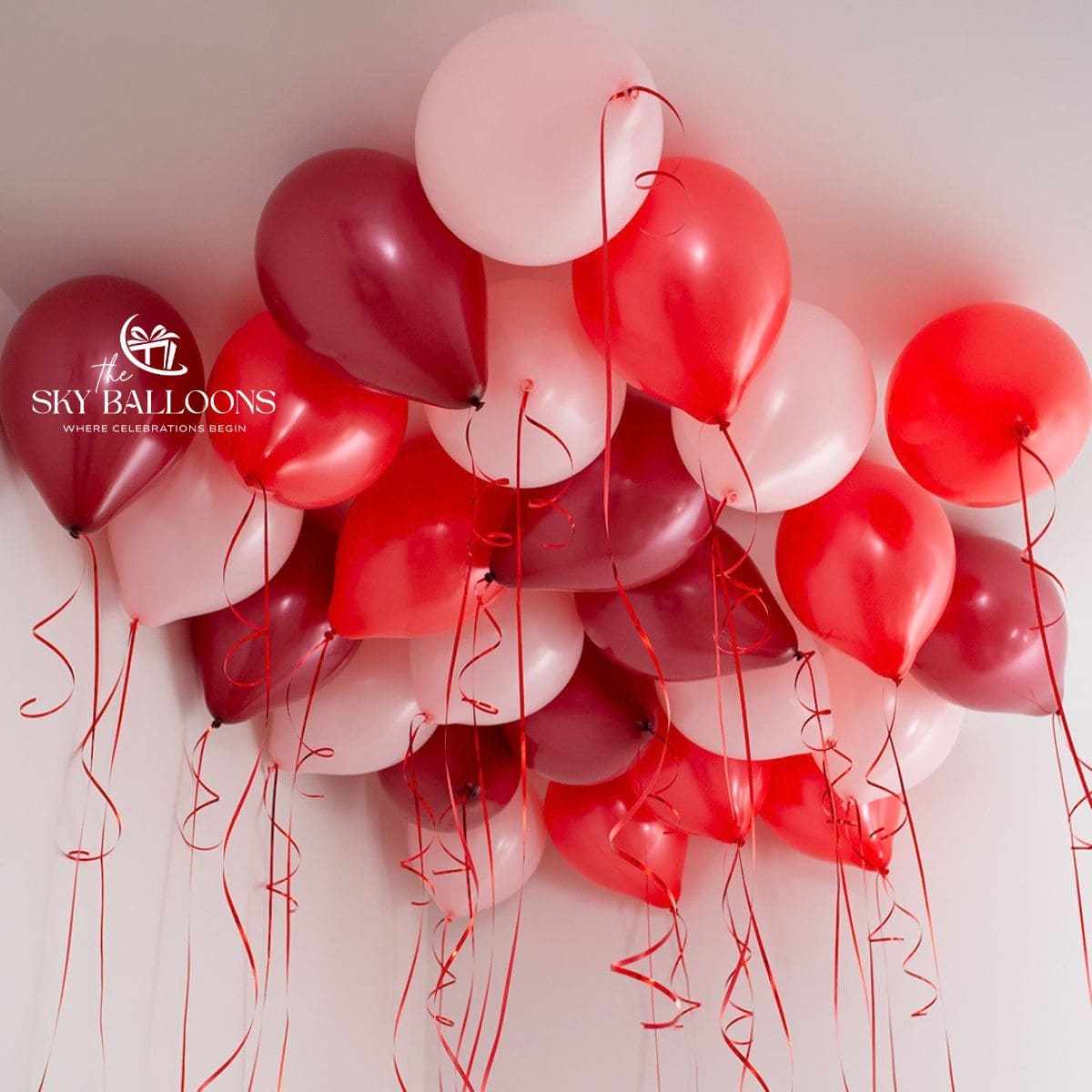 Red, burgundy and blush-pink helium ceiling balloons with hanging red curling ribbons.