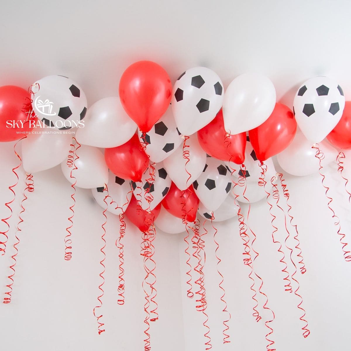 Red and white helium ceiling balloons, including white balloons with black football prints, with hanging red curling ribbons.