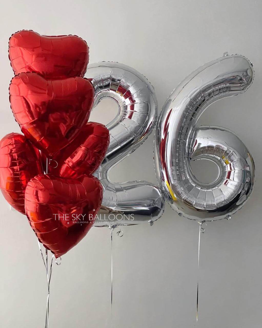 Red heart-shaped balloons and silver number '26' balloon against a white background