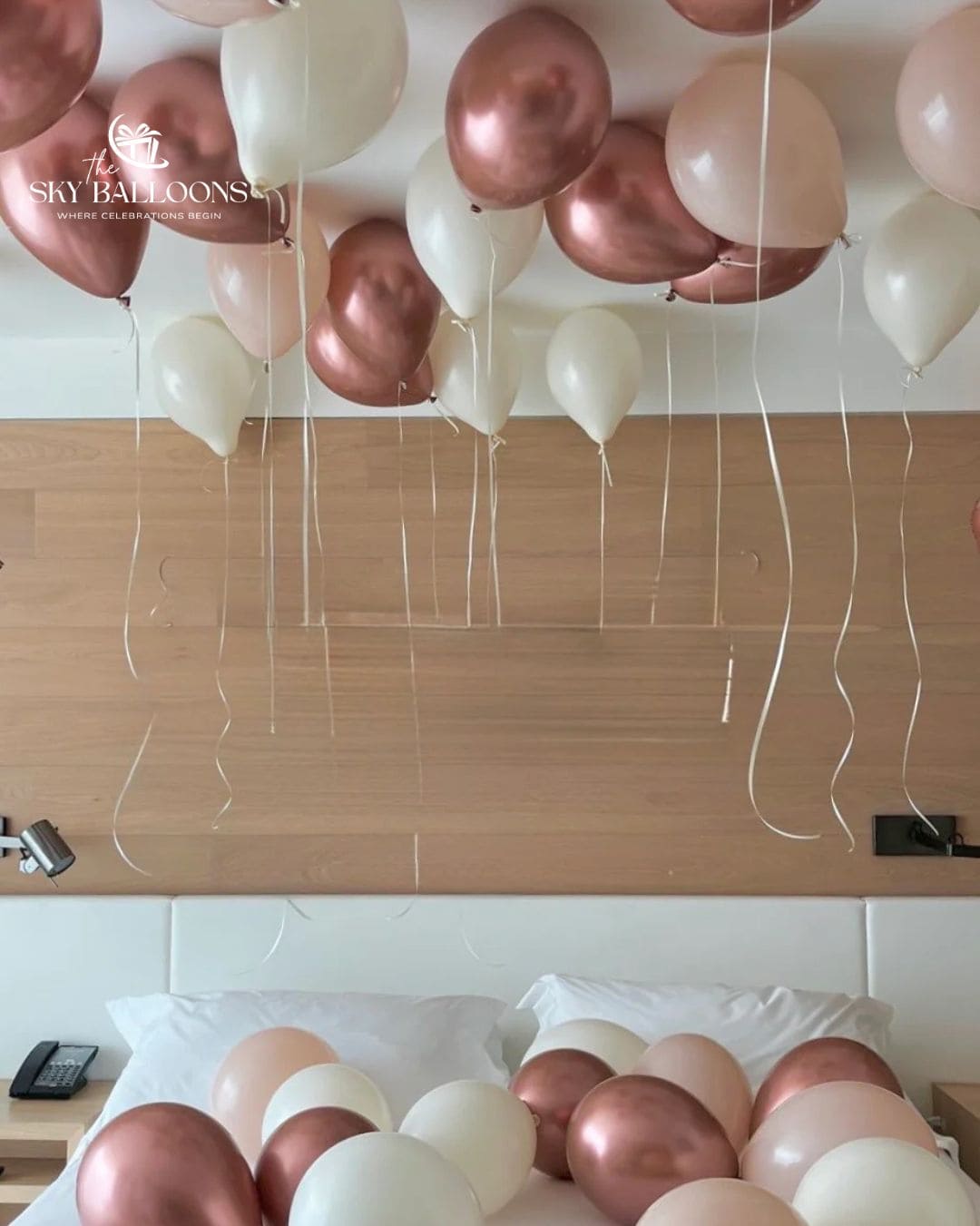 Bedroom balloon decoration with metallic rose gold, blush pink and cream balloons floating on the ceiling with hanging ribbons and scattered across the bed.