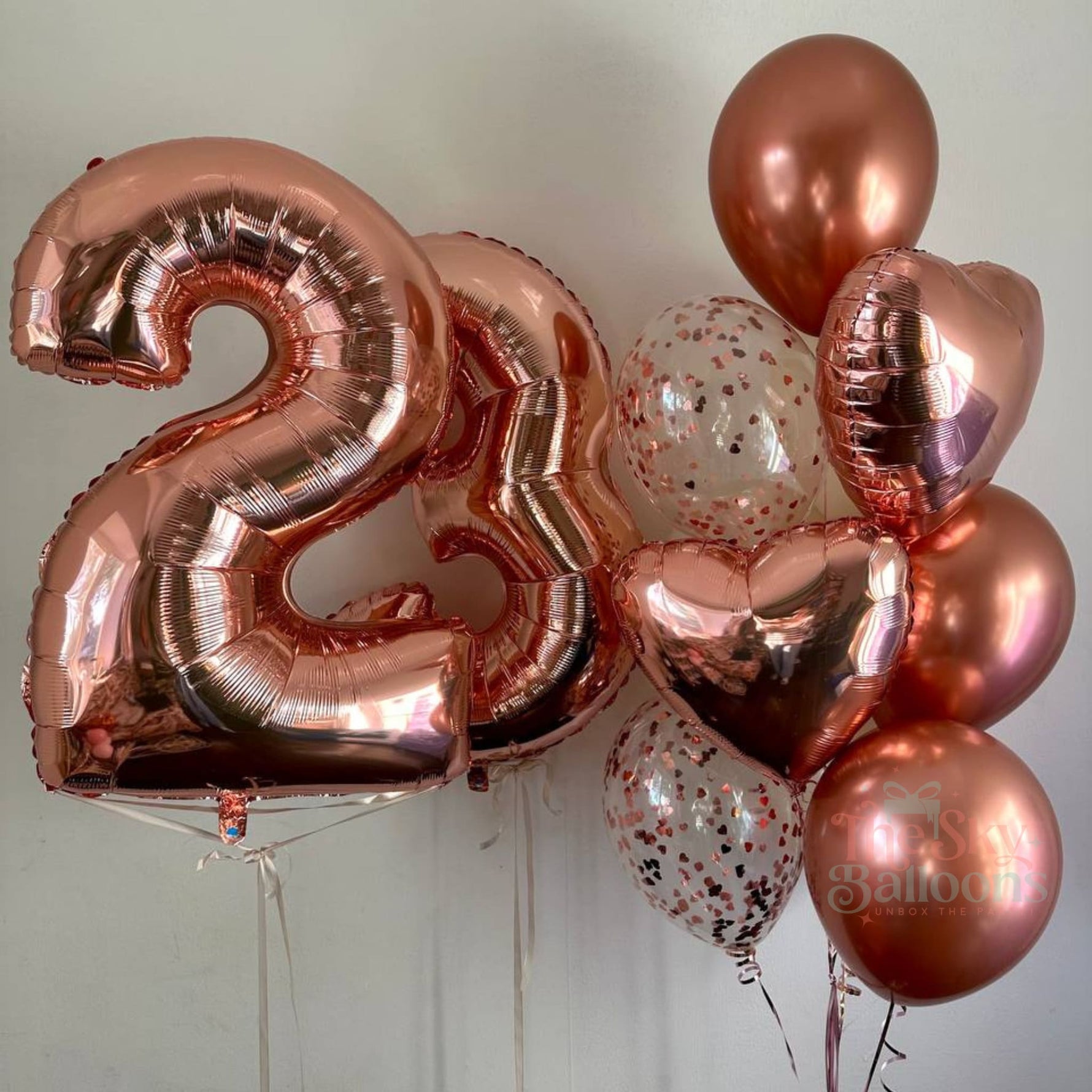 Rose gold number '23' balloon and other balloons against a light background