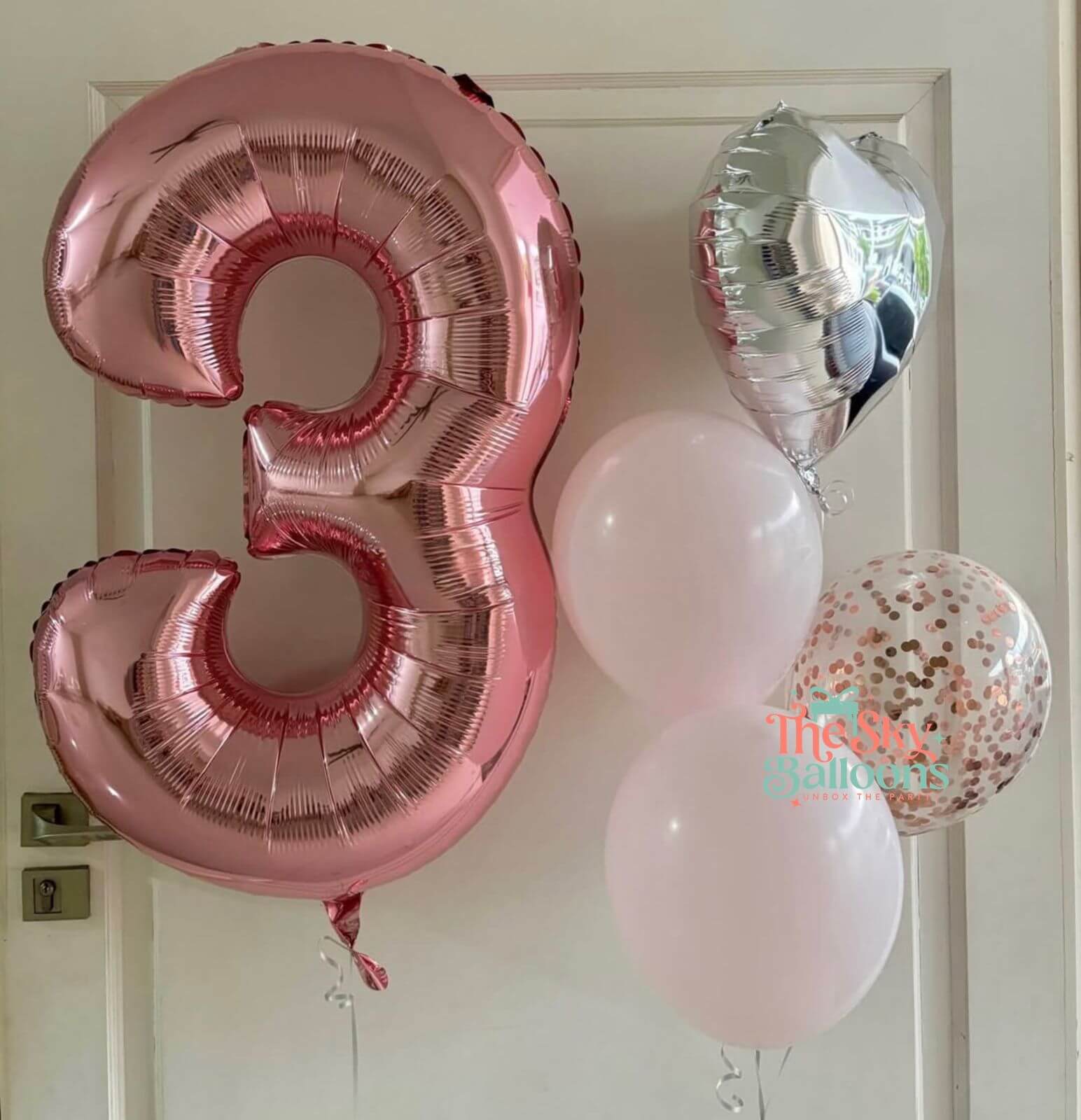 Pink number 3 balloon and other balloons against a white door