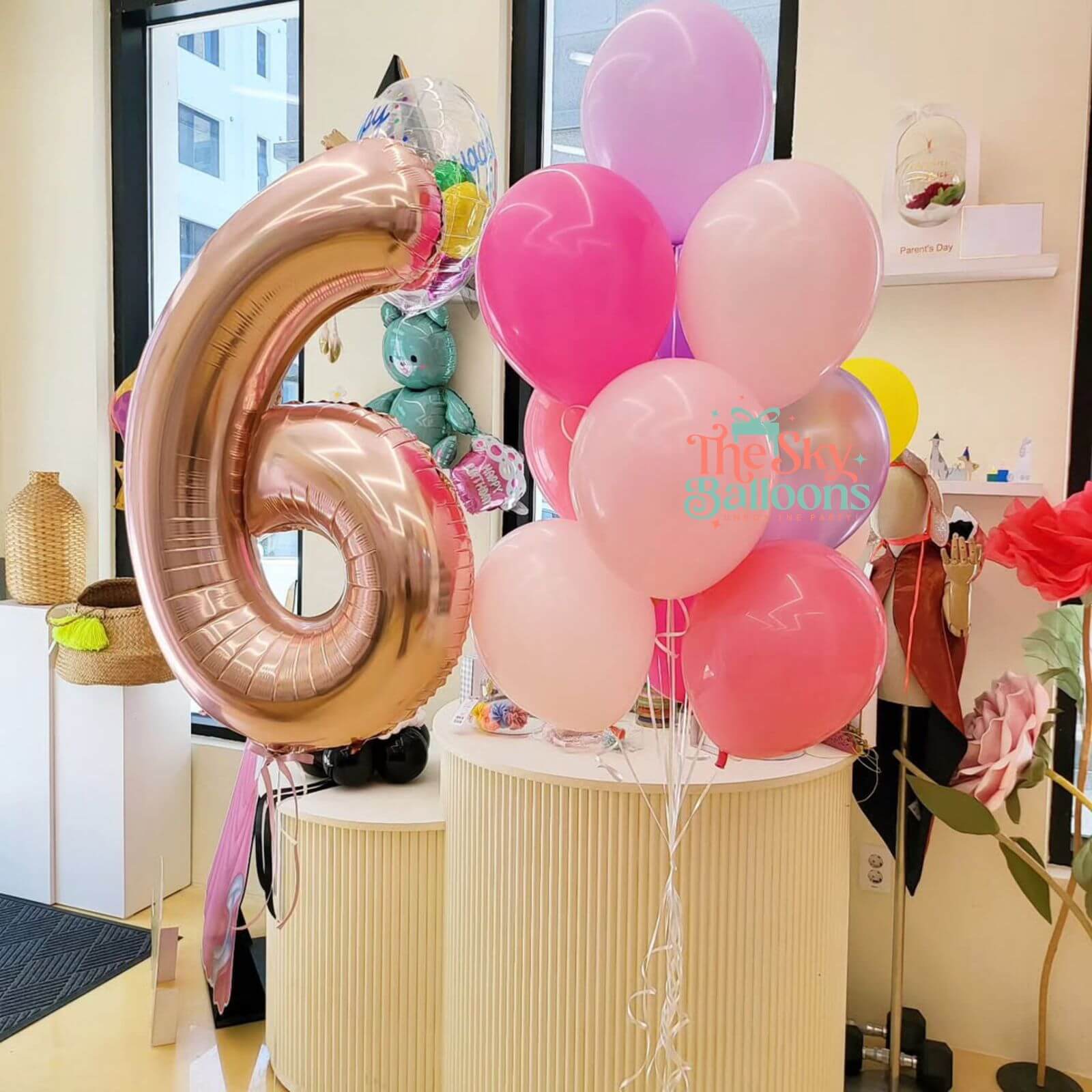 Pink balloons with a number 6 balloon and teddy bear in a room.