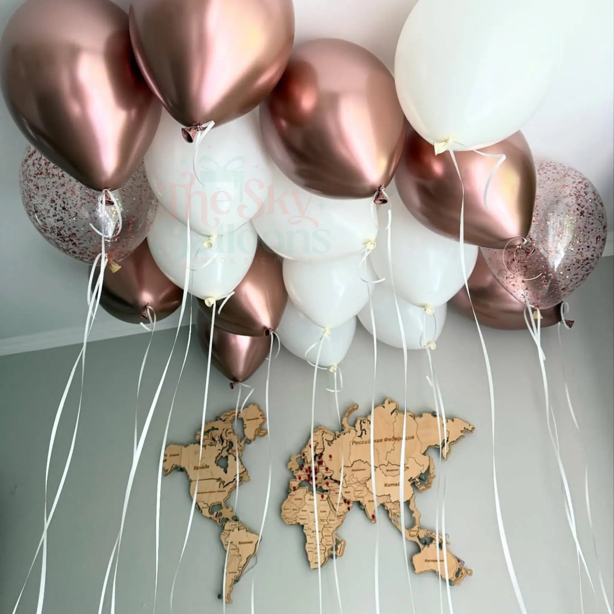 Rose gold and white balloons with string tied to a world map on a light gray wall.