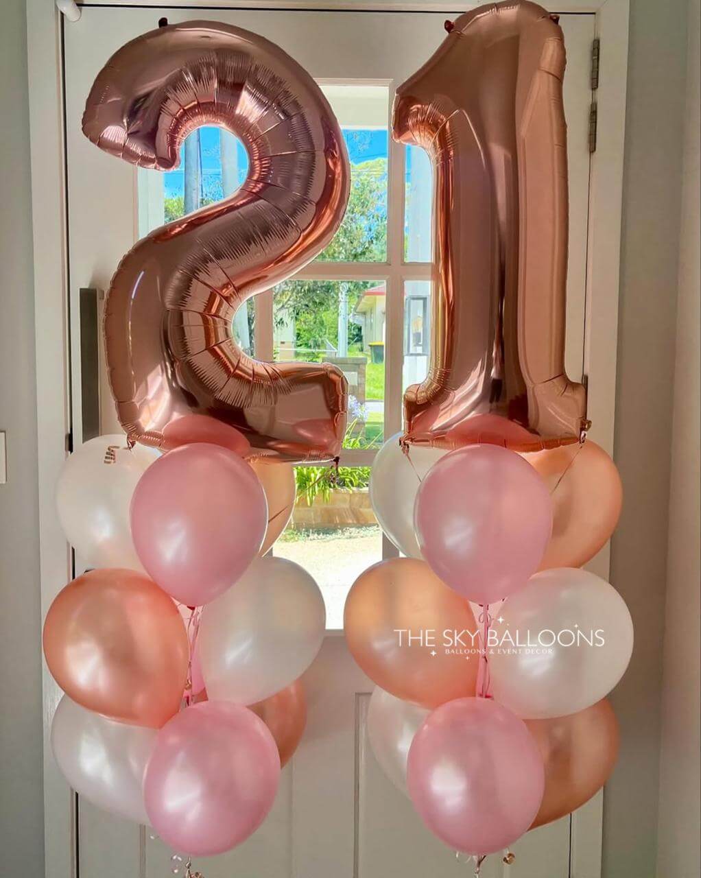 Rose gold number '21' balloons with pink and white balloons against a door background.
