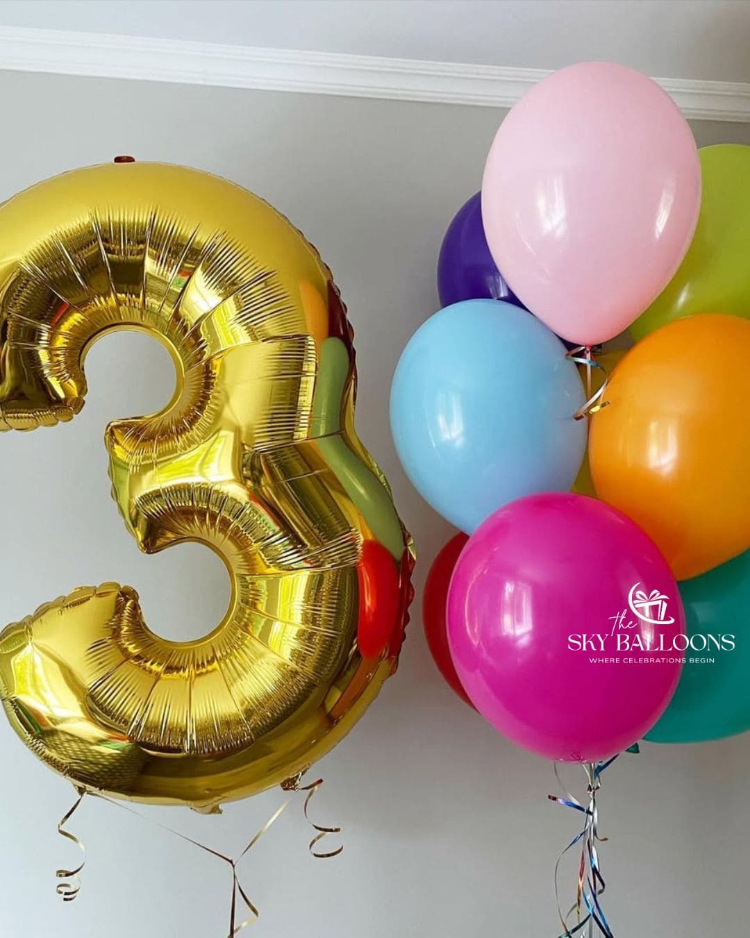 Gold number 3 foil balloon beside a colourful bouquet of pink, blue, orange, purple, lime green, red and teal latex balloons.