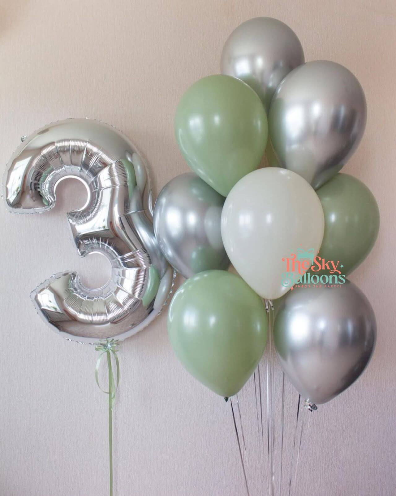 Silver number 3 balloon and green and silver balloons against a light background