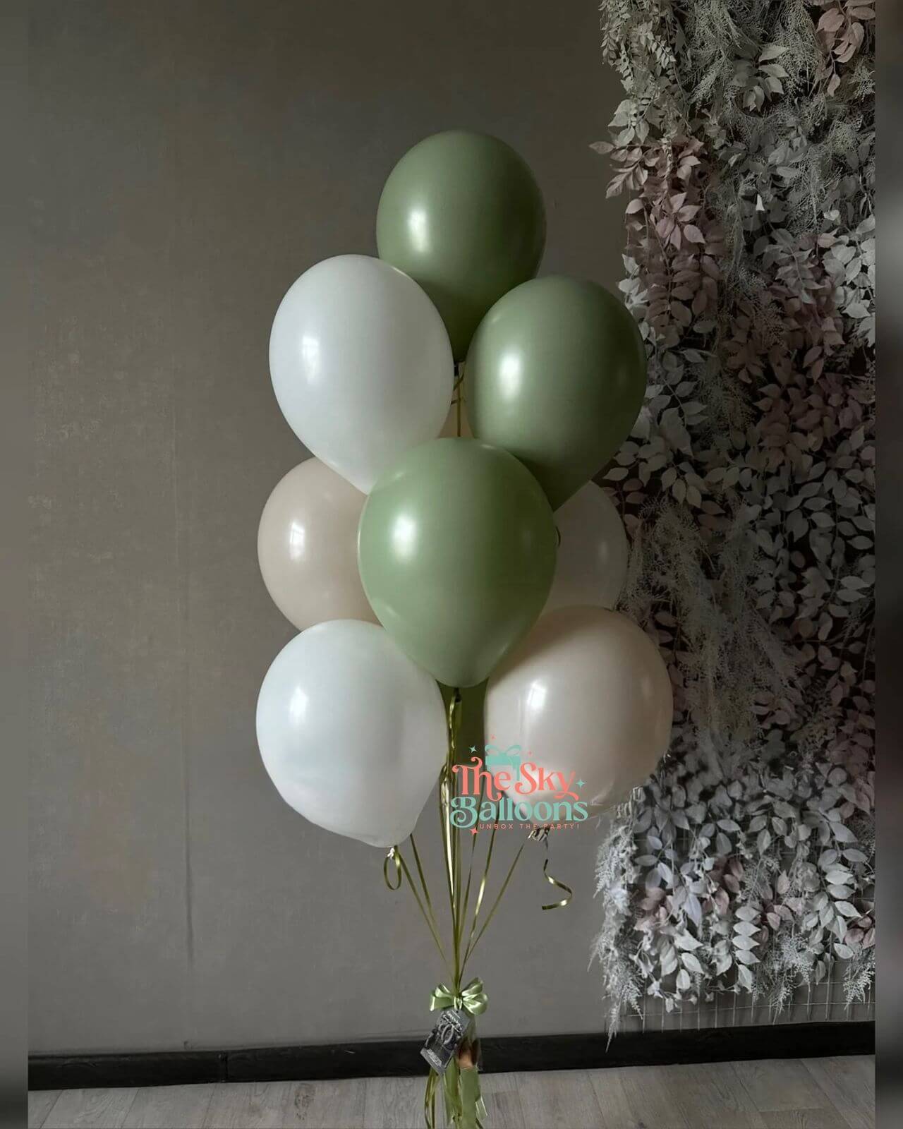 Bunch of green and white balloons tied together with a decorative bow against a textured wall.