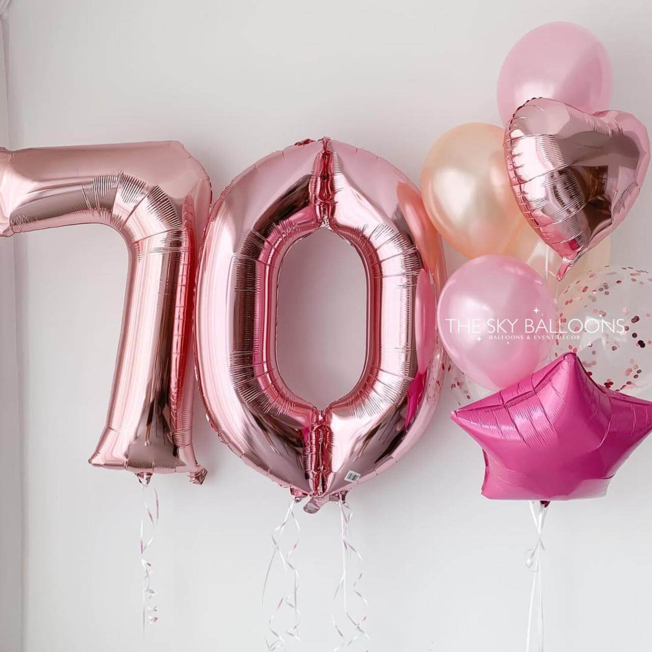 Rose gold number balloons spelling '70' on a white background with additional pink balloons.