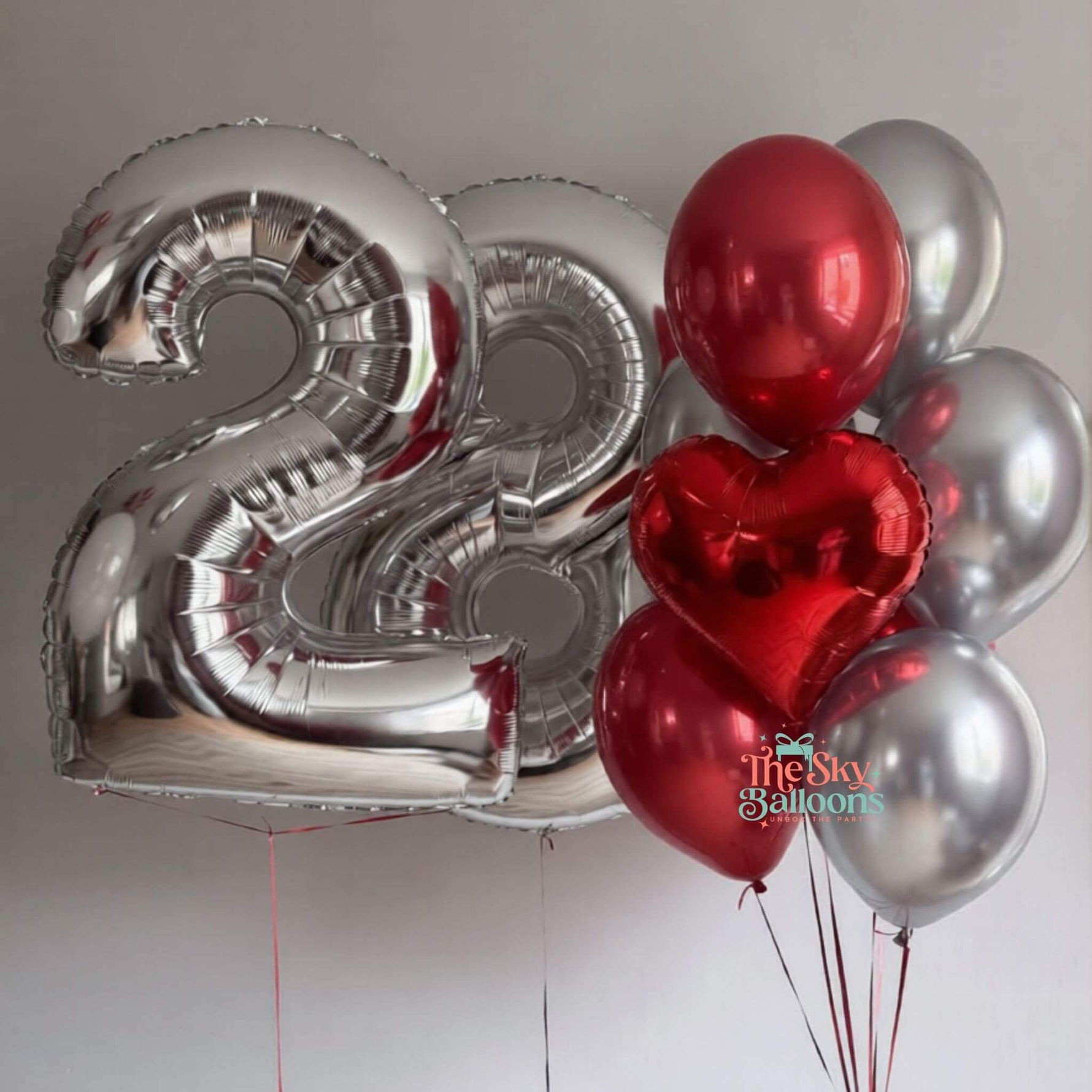 Silver number 22 balloon and red and silver heart-shaped balloons on a plain background