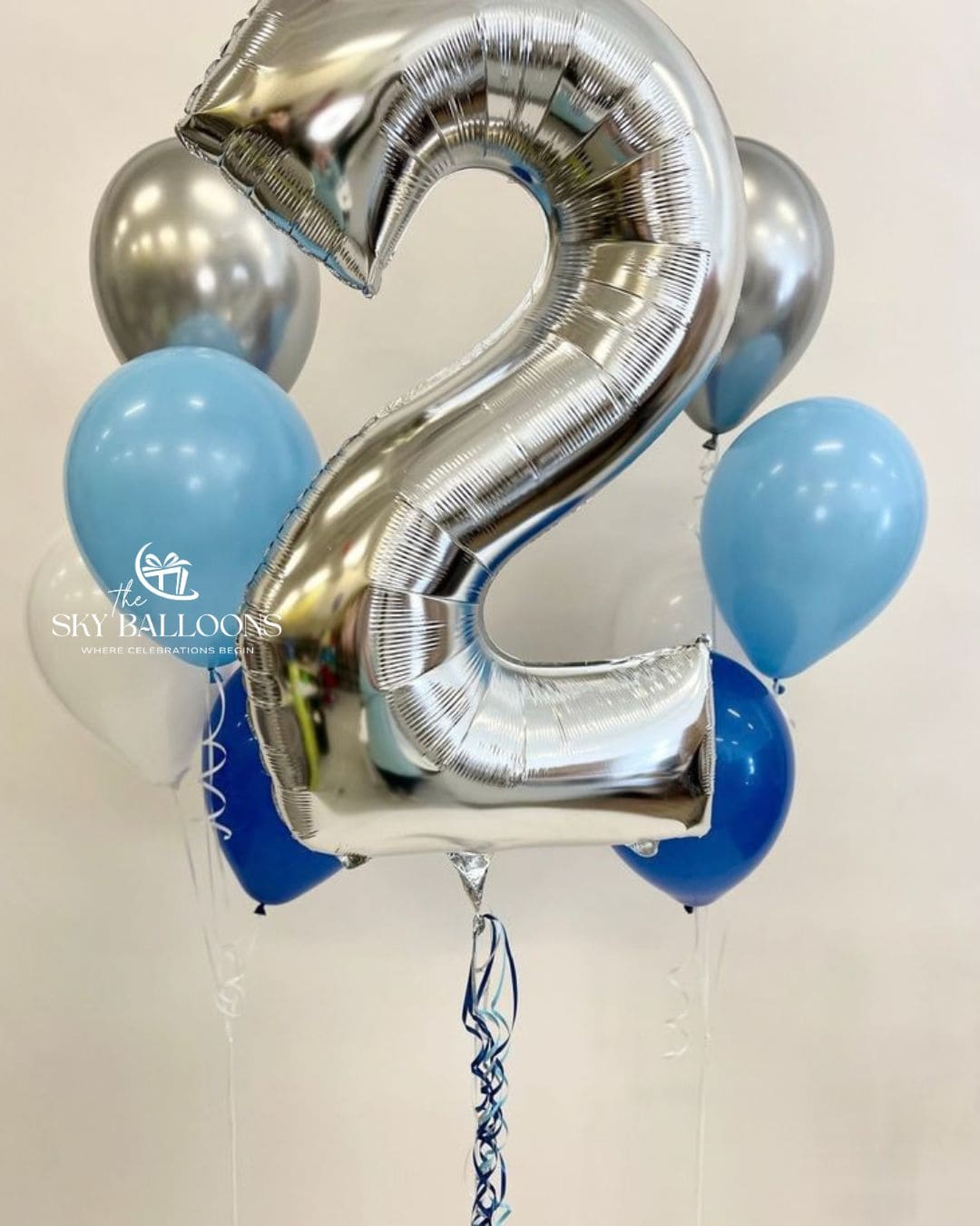 A metallic silver foil balloon shaped like the number 2, surrounded by light blue, dark blue, and silver latex balloons.