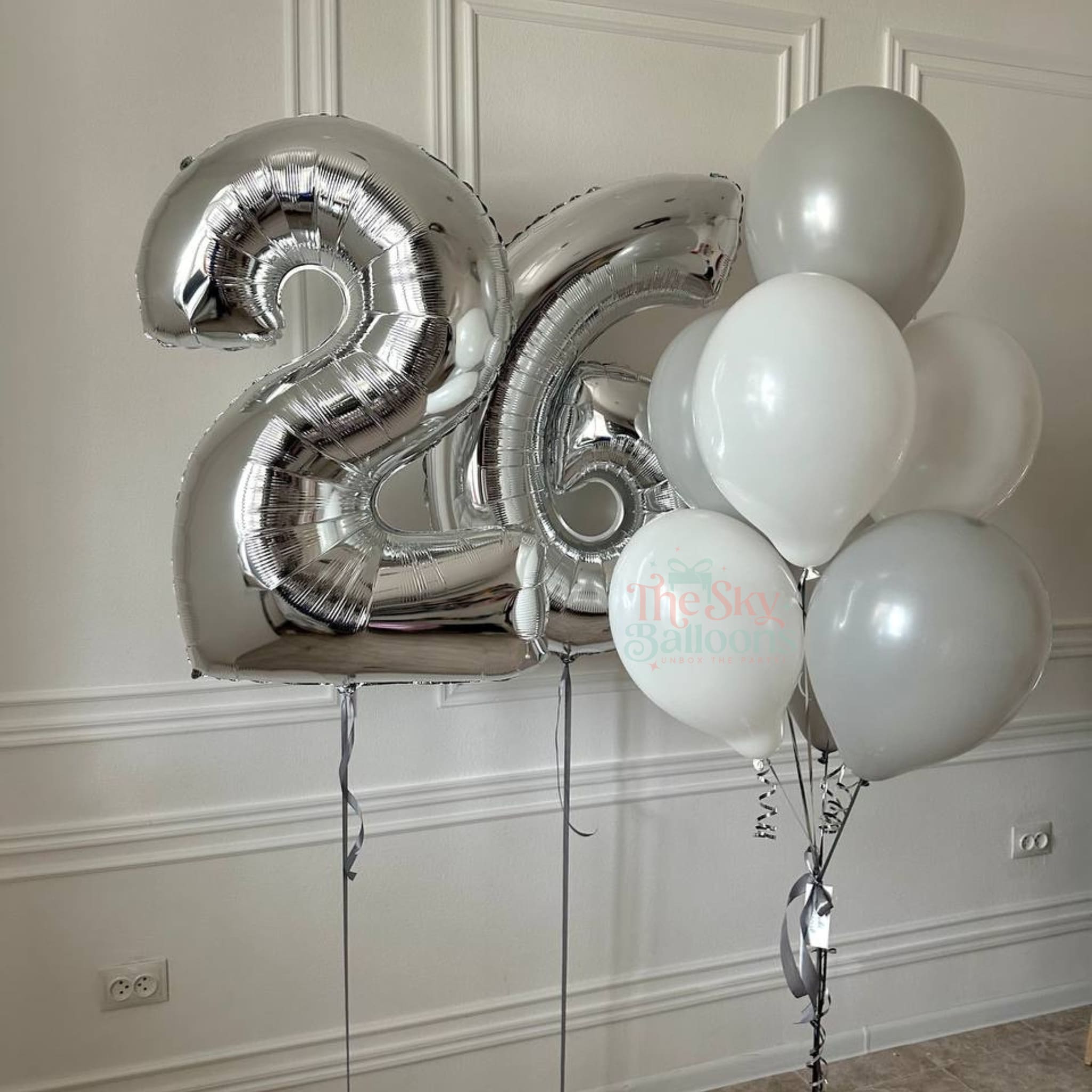 Silver number 26 balloon and white balloons against a white wall.