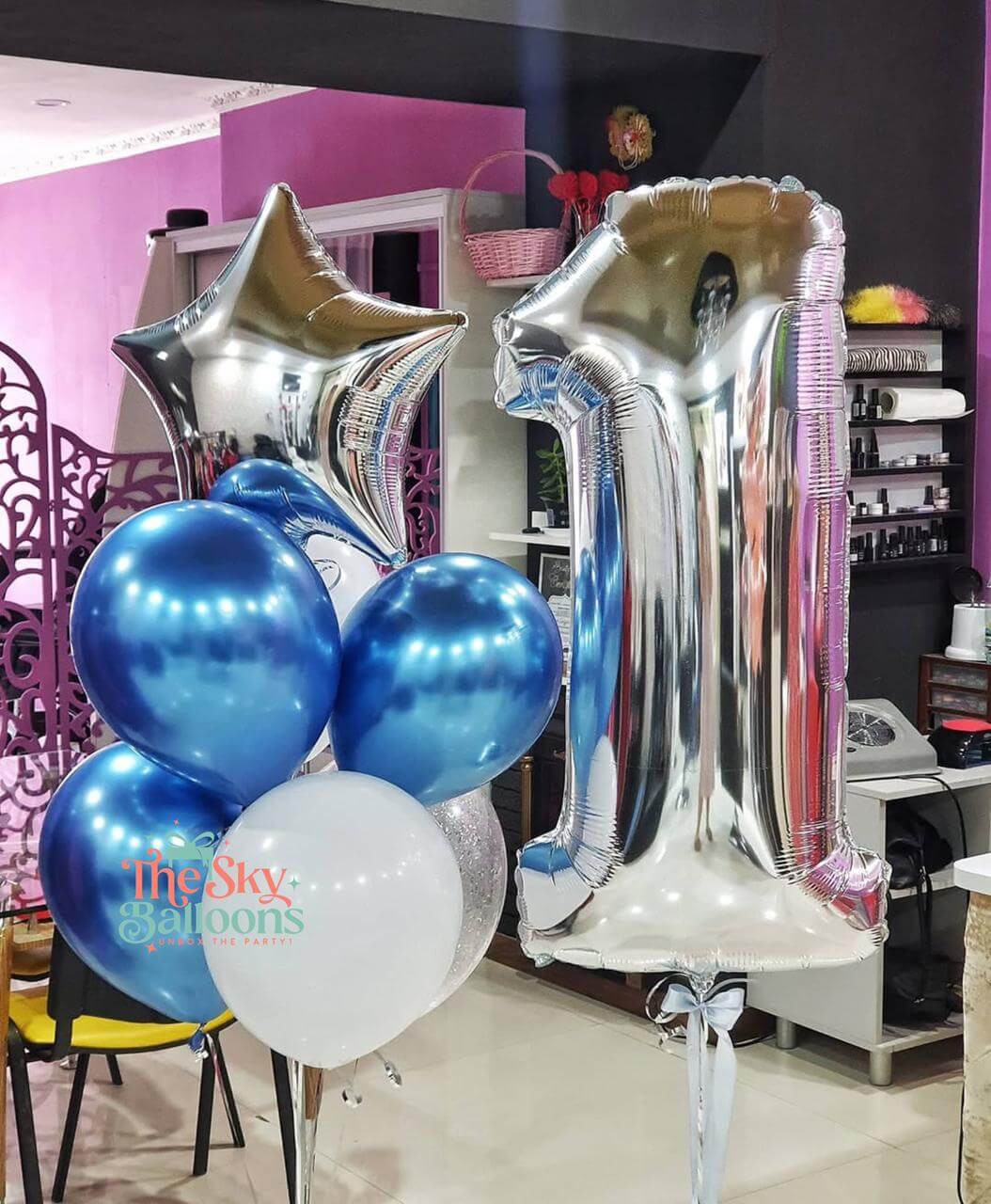 Silver number 1 balloon and blue and white balloons in a room with pink walls.