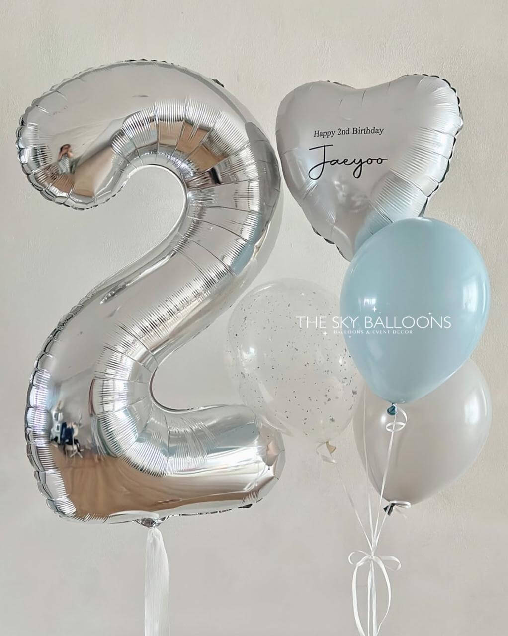 Silver number 2 balloon, heart-shaped balloon with 'Happy 2nd Birthday' text, and light blue balloon on a white background.