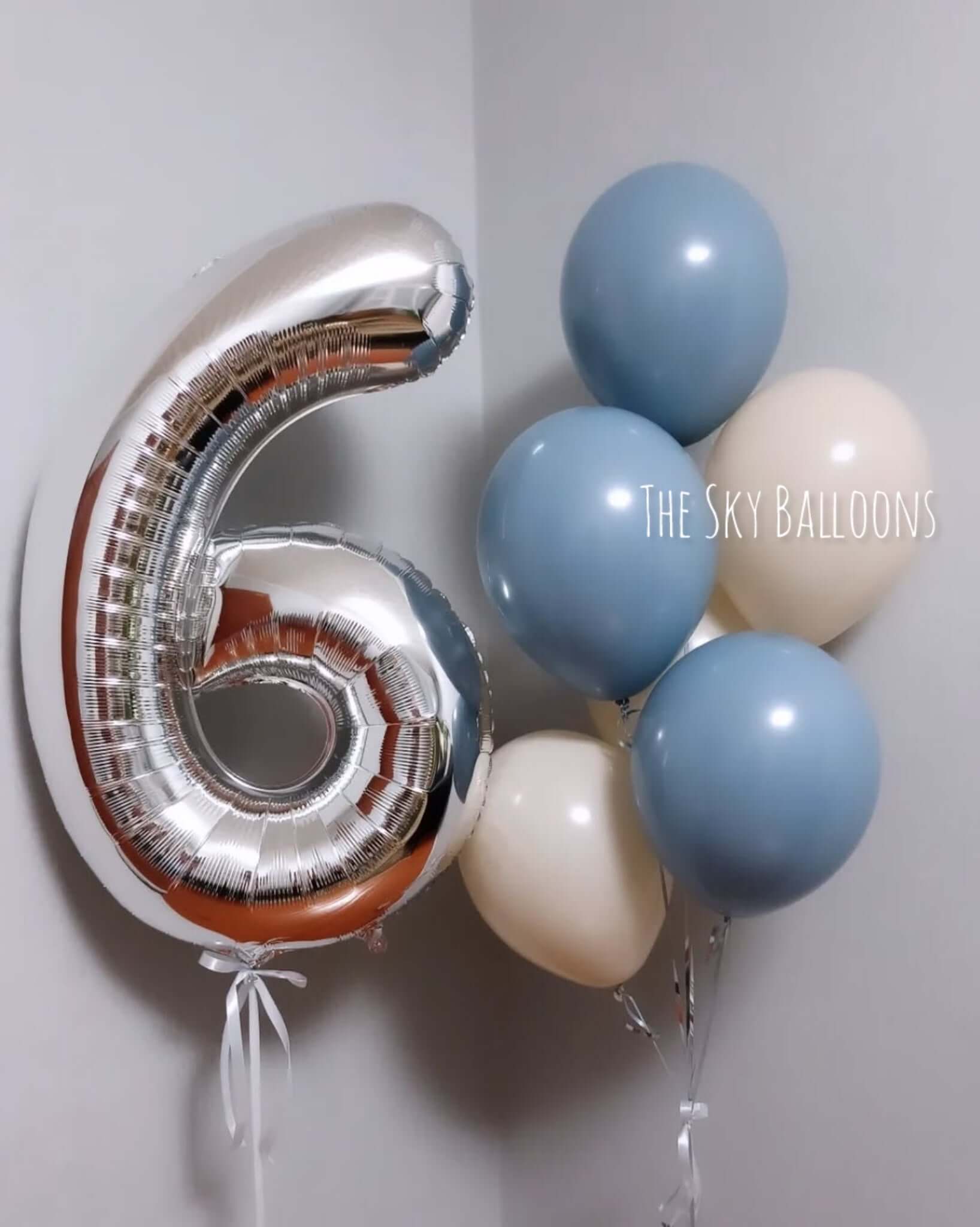 Silver number 6 balloon and blue and white balloons against a light gray background.