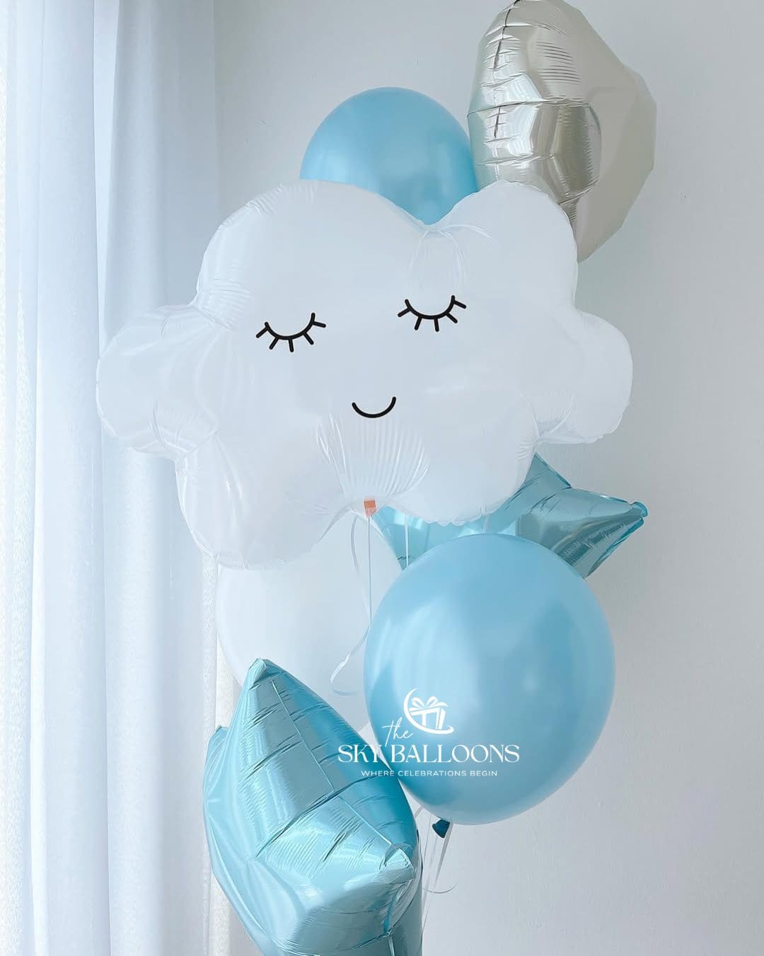 Balloon bouquet with a smiling white cloud foil balloon, light blue latex balloons, blue star foil balloons and a silver heart foil balloon.⠋