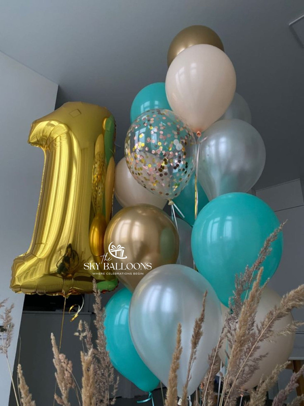 Gold number 1 foil balloon with teal, cream, chrome gold, silver and clear confetti balloons arranged for a birthday celebration.
