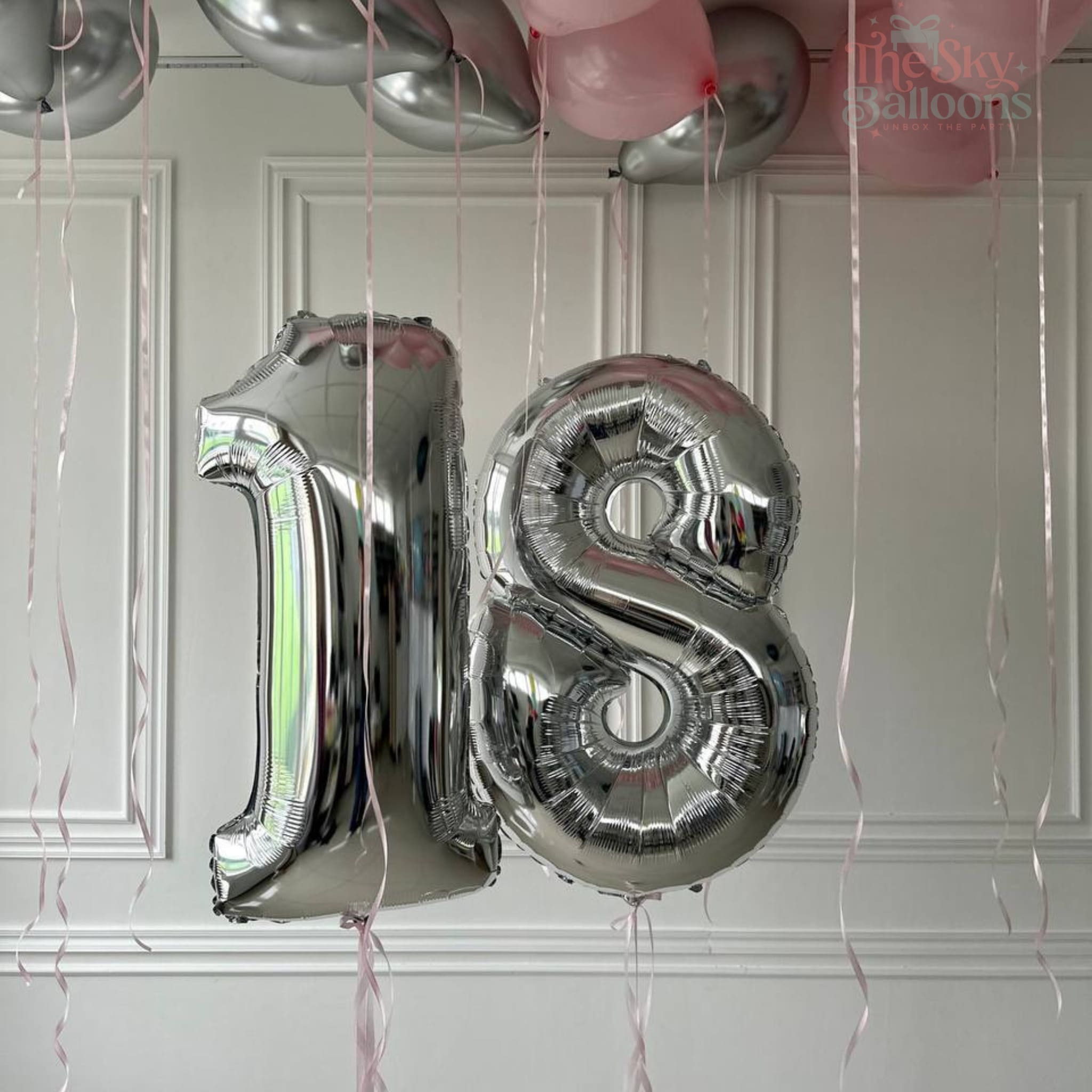 Silver '18' balloons against a white paneled wall with pink and silver balloons.