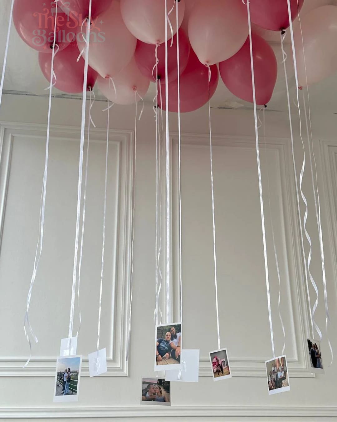 Pink and red balloons with string attached to a white wall.