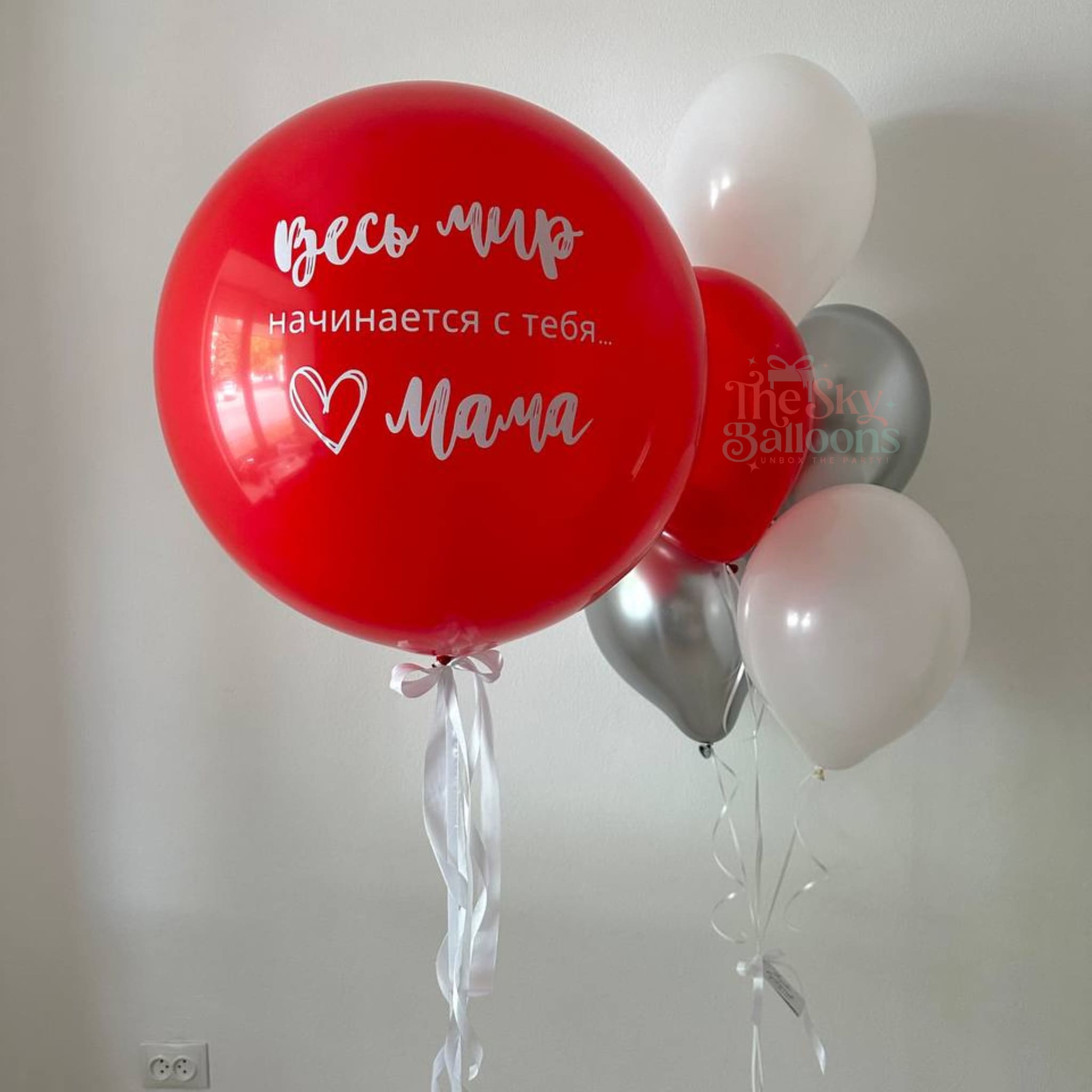 Red balloon with text and heart design, surrounded by other balloons against a plain background