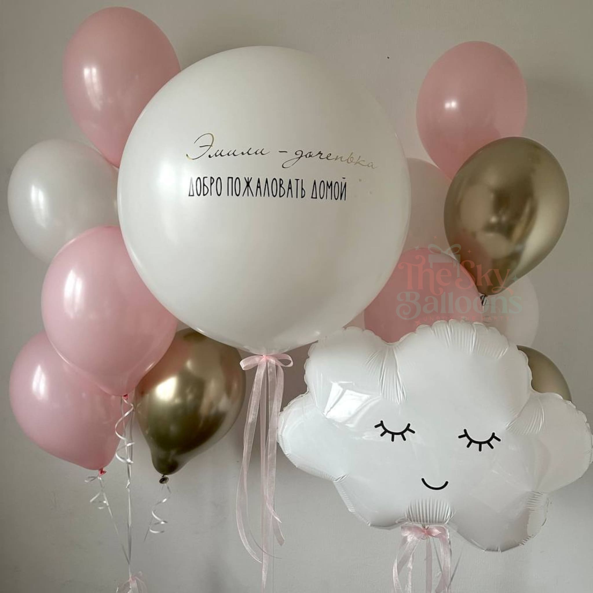 Decorative balloon arrangement with pink, white, and gold balloons, including a cloud-shaped balloon with a face.