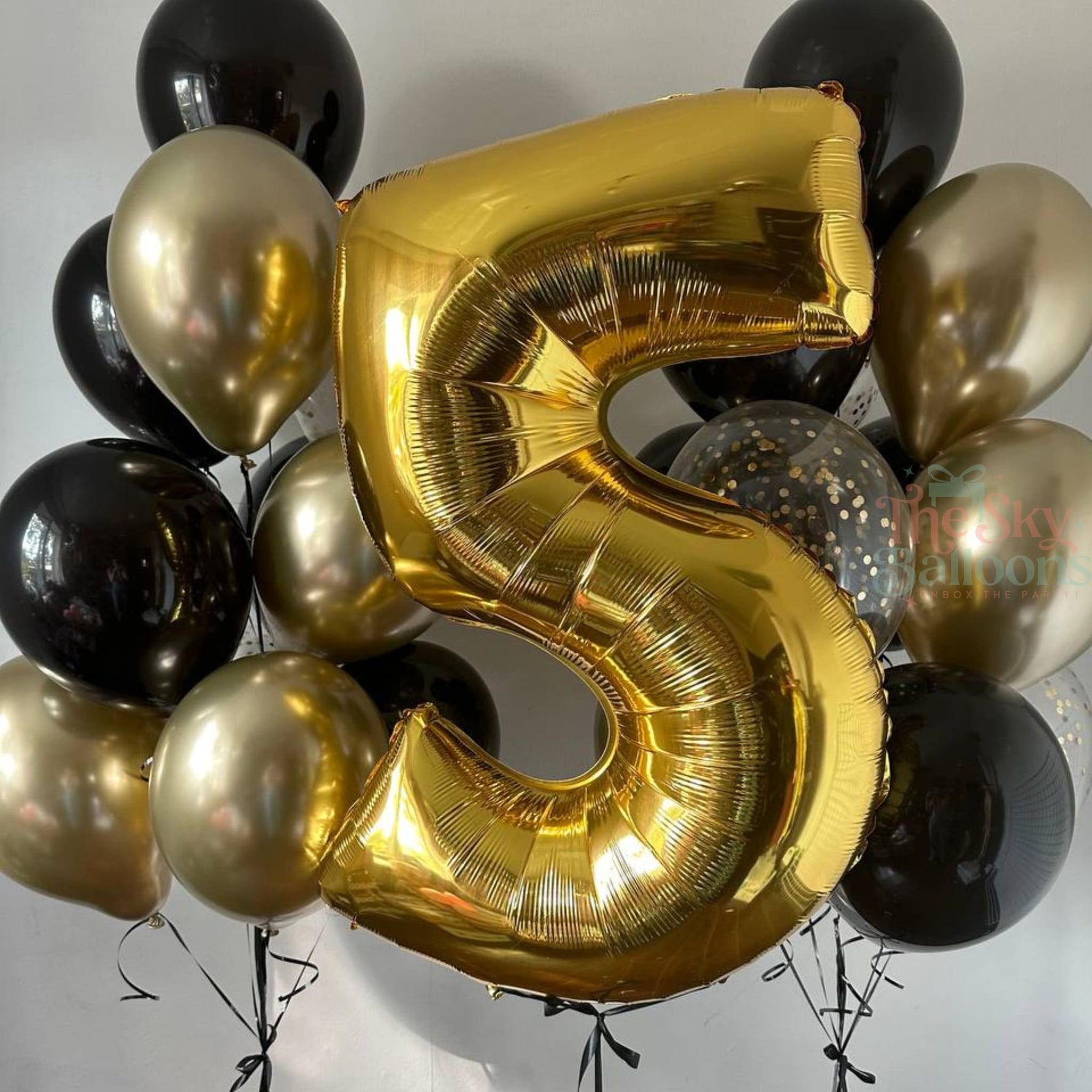 Gold number 5 balloon surrounded by black and gold balloons on a plain background