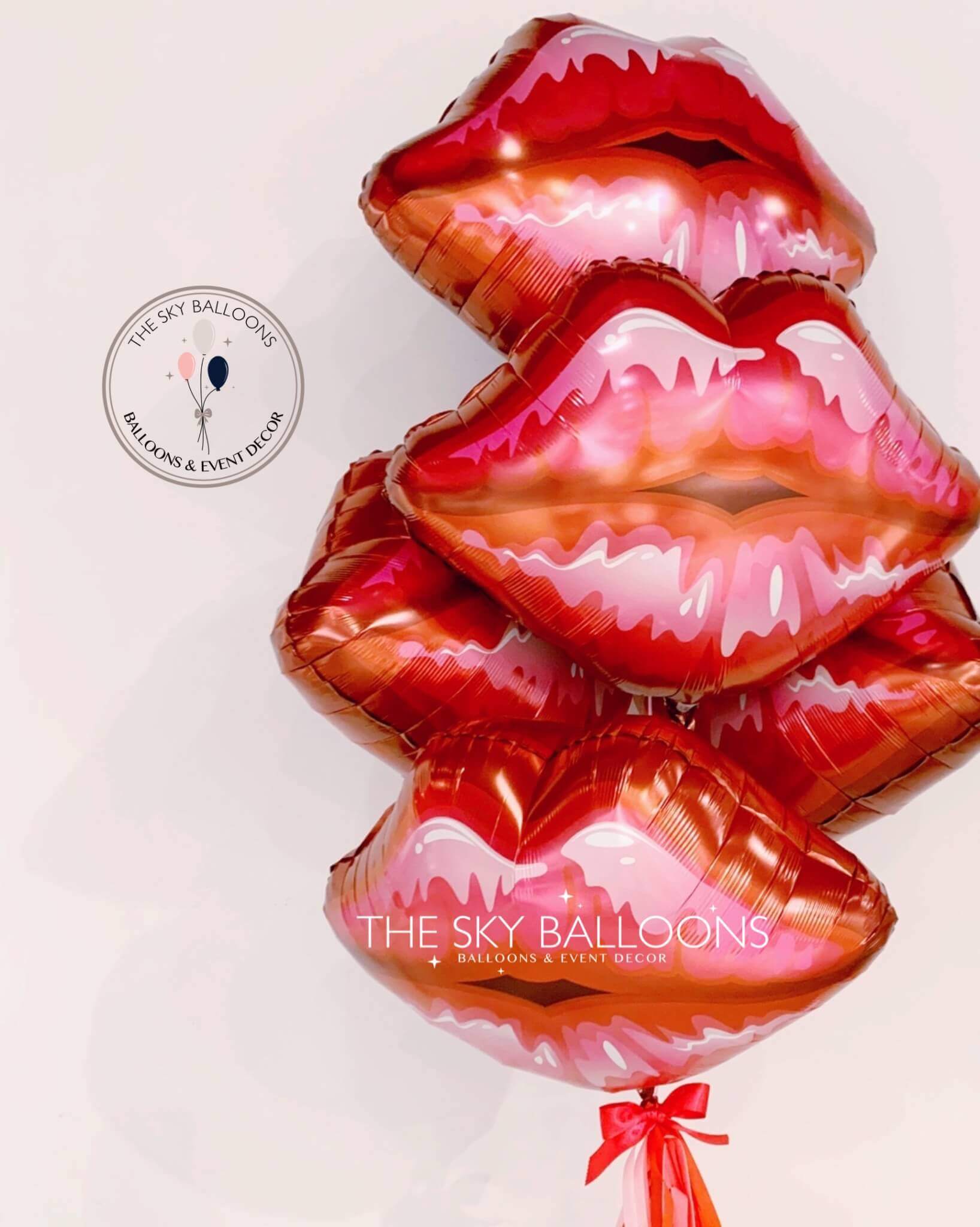 A set of inflated red and pink colored balloons in the shape of lips, with a label at the top left corner reading 'The Sky Balloons'.