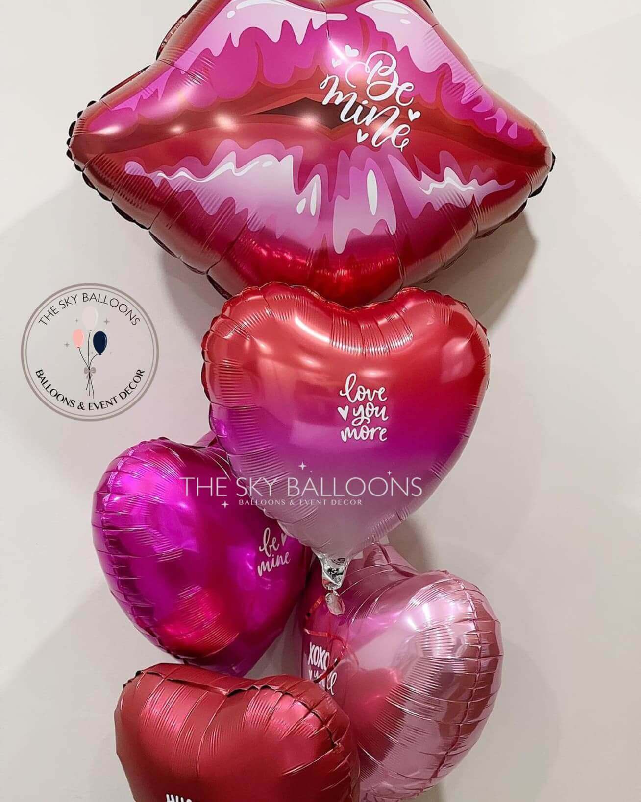 A bouquet of red and pink heart-shaped balloons with customized text, including 'Valentine' and 'I love you', displayed against a neutral background.