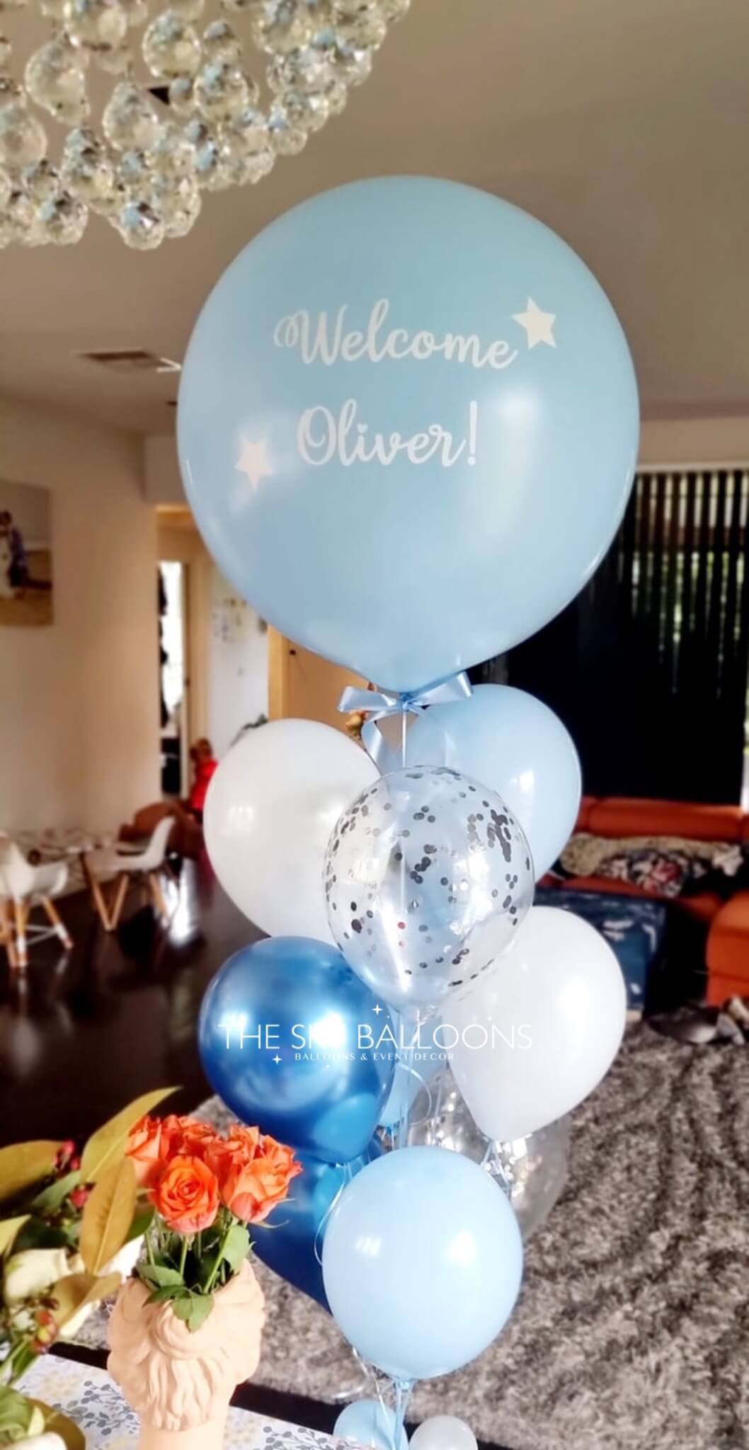 Decorative balloon arrangement with 'Welcome Oliver!' text in a room setting.