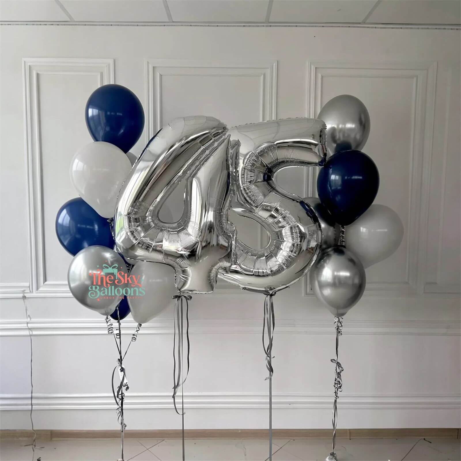 Silver number '45' balloon with blue and white balloons against a white wall.