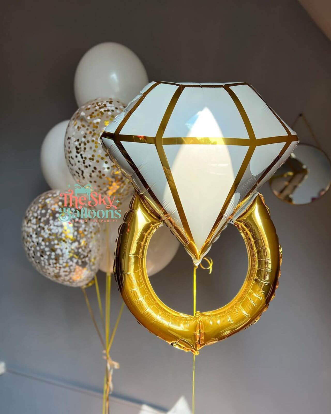 Decorative balloons including a diamond-shaped and a heart-shaped gold balloon with white balloons in the background.