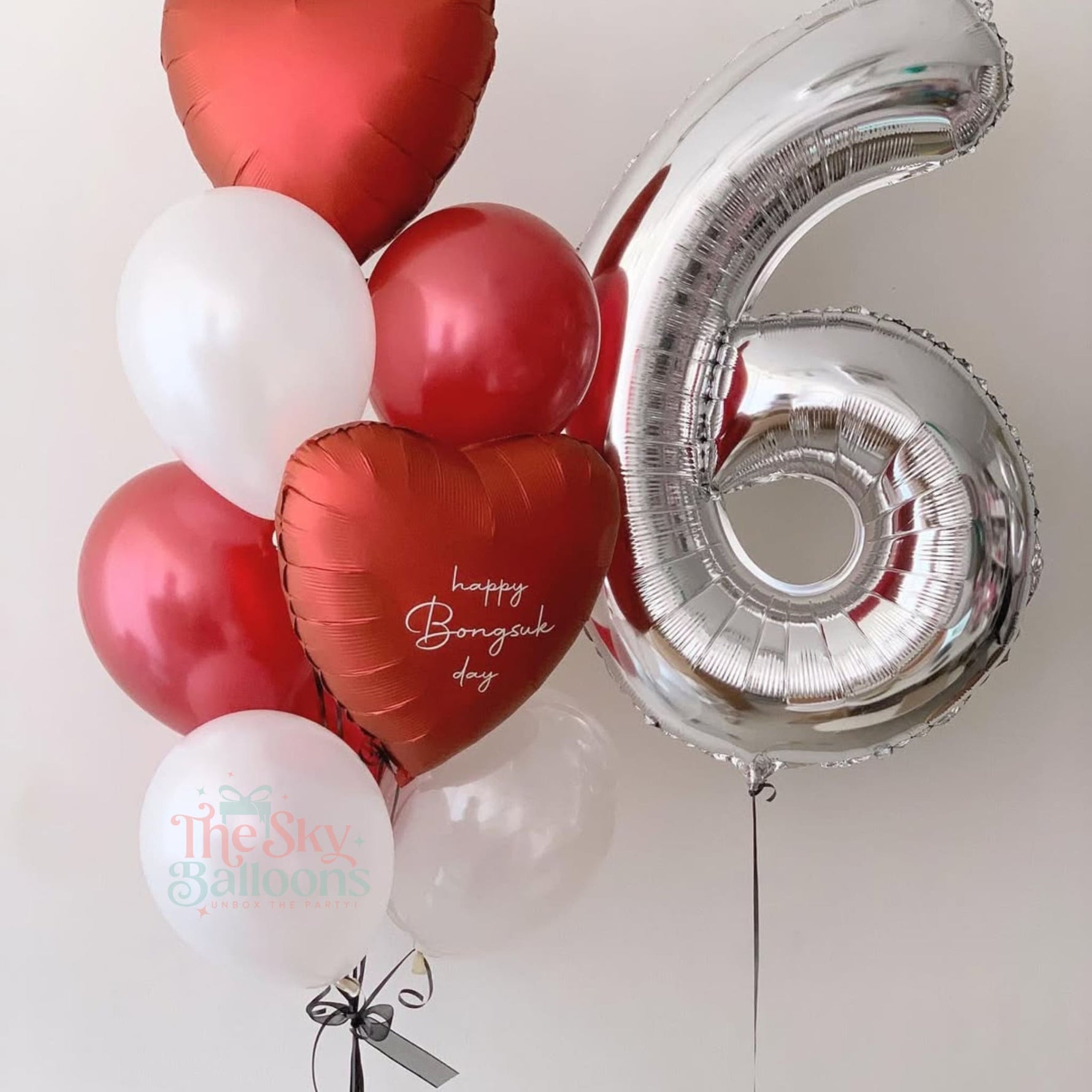 Balloon bouquet with red heart-shaped balloons, a silver number 6 balloon, and white balloons with text on a light gray background.