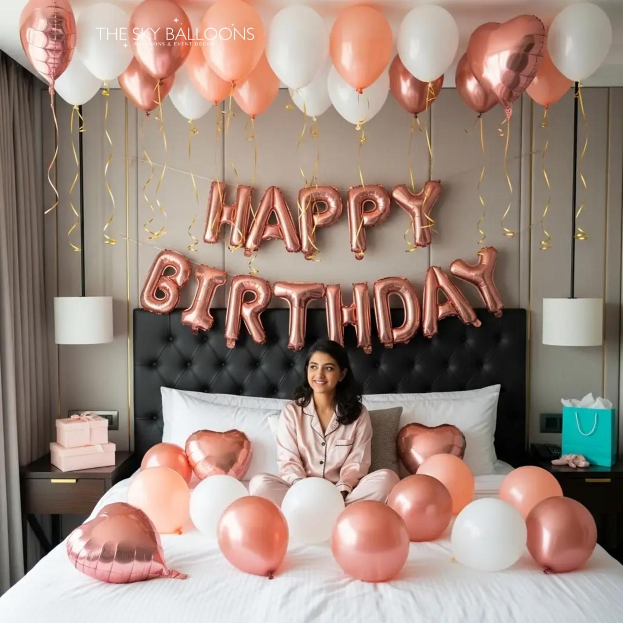 Woman sitting on a bed with 'Happy Birthday' balloons and decorations in a bedroom setting.