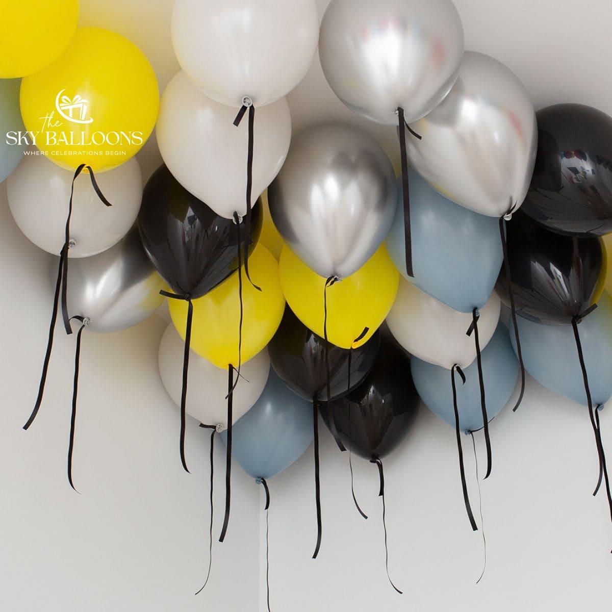 Yellow, pale-blue, white, black and chrome-silver helium ceiling balloons with hanging black ribbons.
