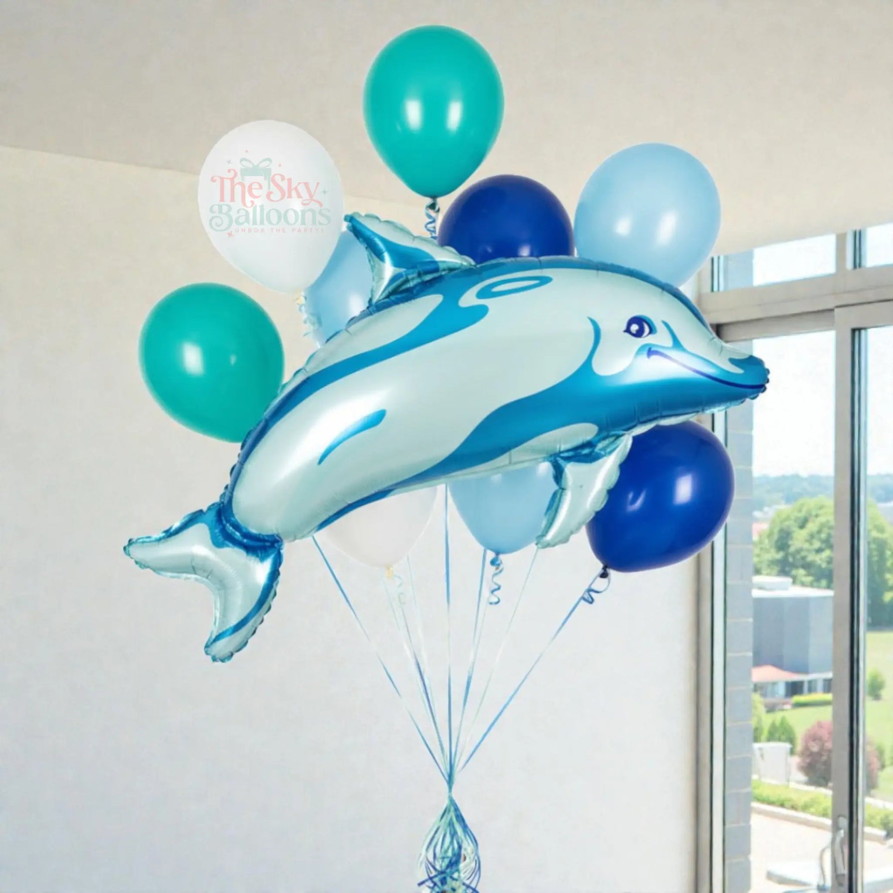 Dolphin-shaped balloon with other balloons in a room with a window.