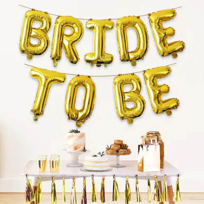 Gold 'BRIDE TO BE' balloons above a dessert table with a cake.
