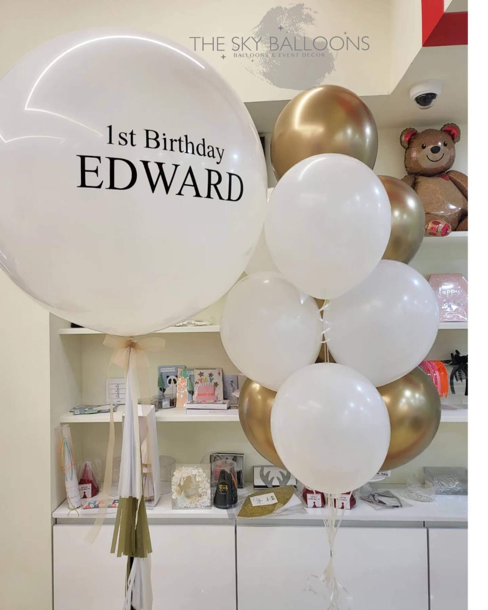 A balloon bouquet featuring a customized '1st Birthday' balloon with the name 'Edward' printed on it, along with several other latex balloons in varying sizes.