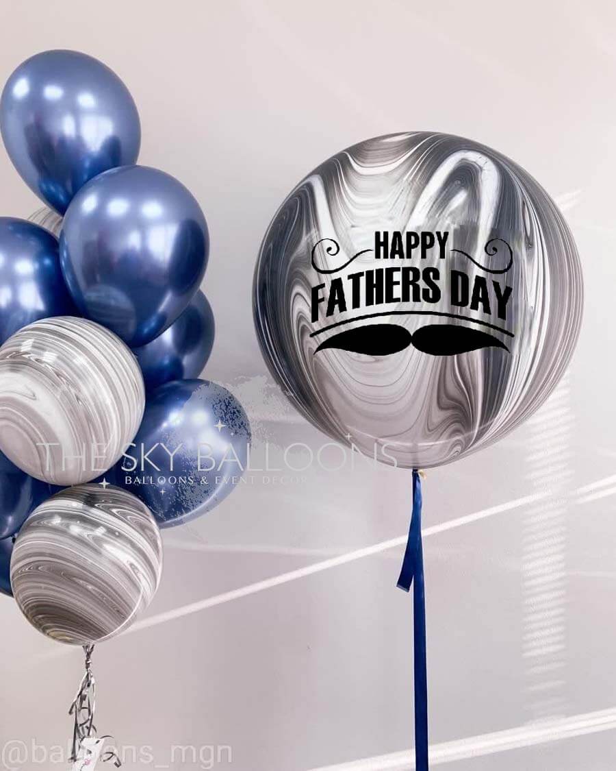 A bouquet of round, silver-colored balloons with the text 'Happy Father's Day' printed on one of them, alongside a large customized balloon with a 'Happy Father's Day' message and a graphic of a mustache.