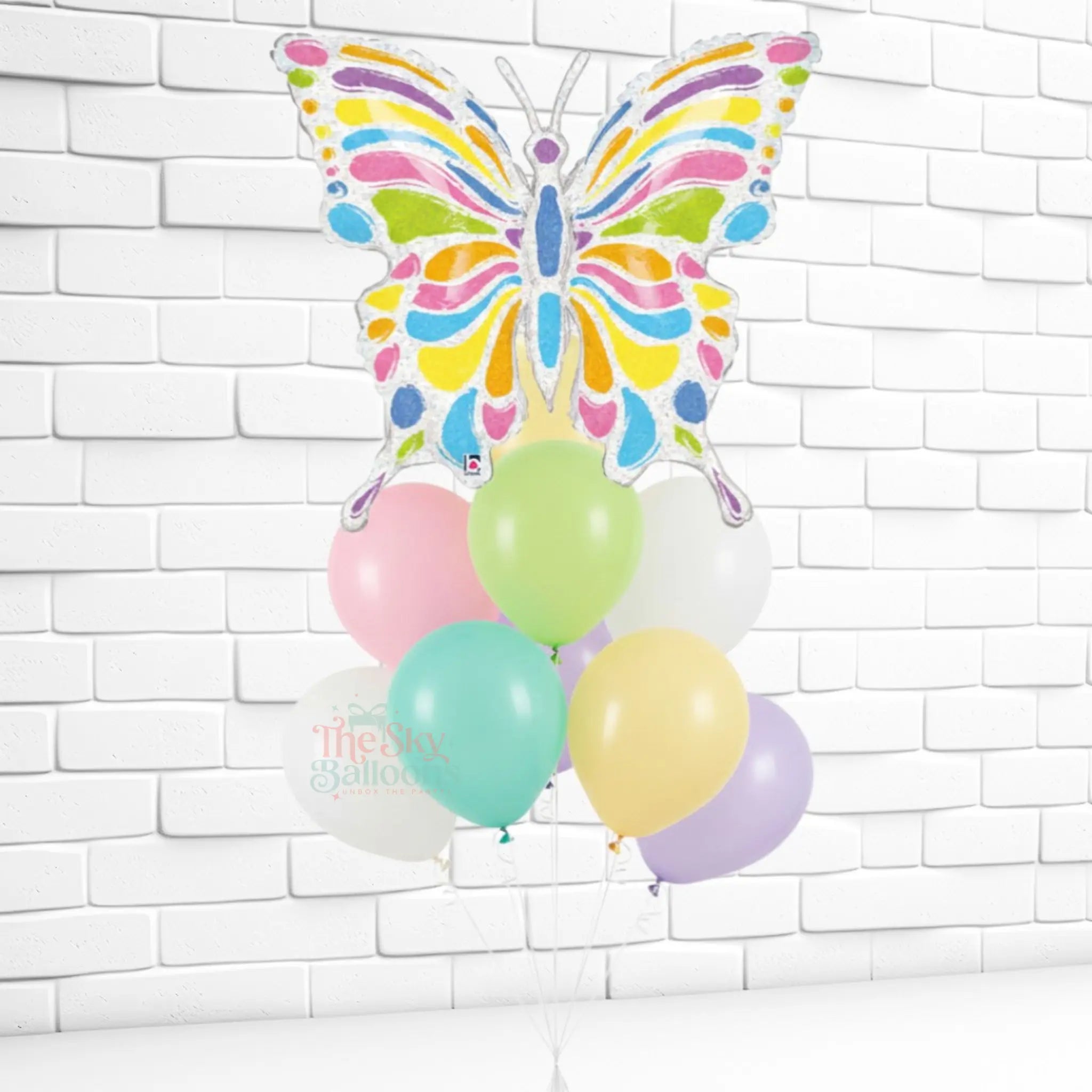 Colorful butterfly-shaped balloon with pastel balloons against a white brick wall.