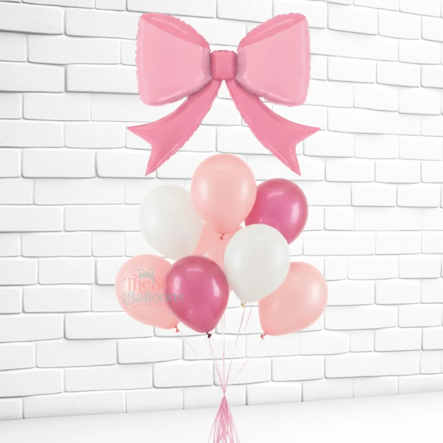 Pink and white balloons with a large pink bow against a white brick wall.