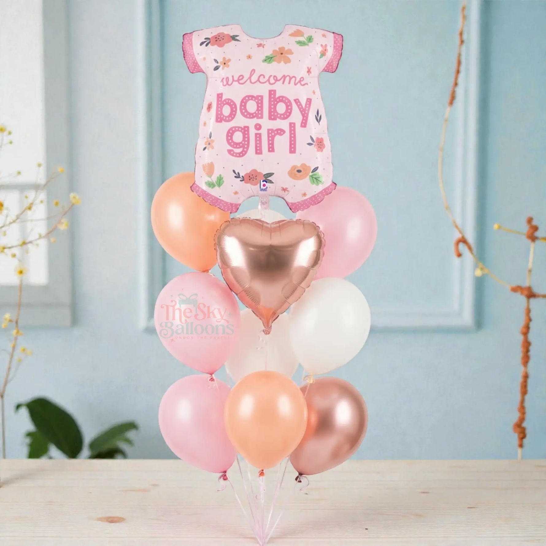 Balloon arrangement with a baby onesie balloon and heart balloon on a light blue background