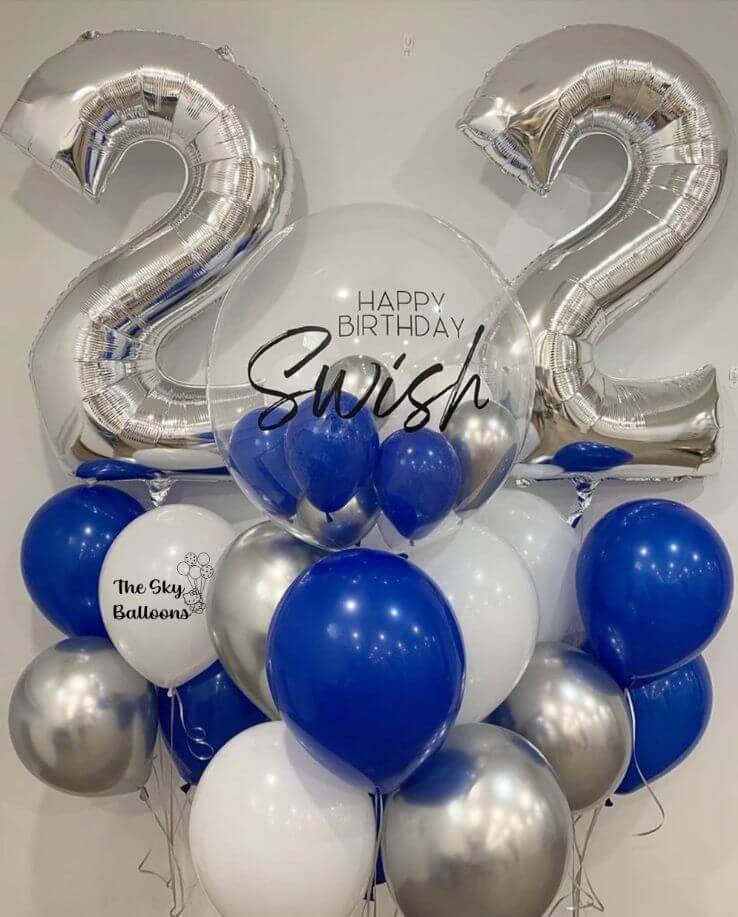 A balloon bouquet featuring silver and blue helium-filled balloons, including large foil numbers '22', a customized balloon with the name 'Swish', and a balloon weight.