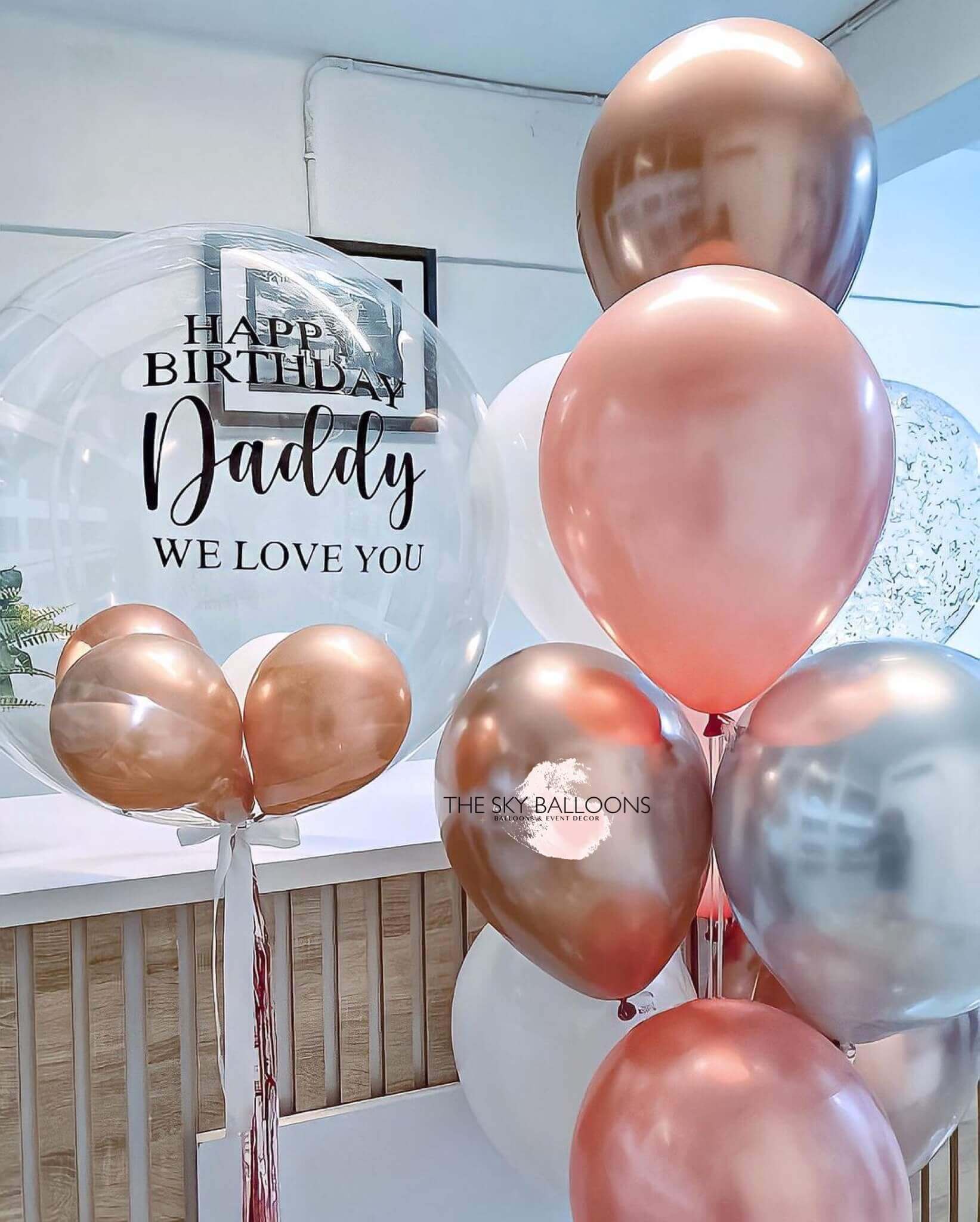 A bouquet of round balloons in shades of pink, silver, and gold, with one balloon featuring a 'Happy Birthday' message and the name 'Daddy', indicating a personalized touch.