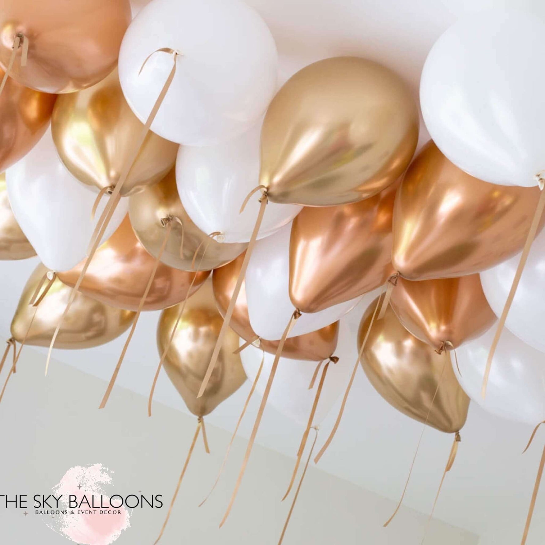 A cluster of helium-filled ceiling balloons in copper, white, and gold colors, tied with strings.